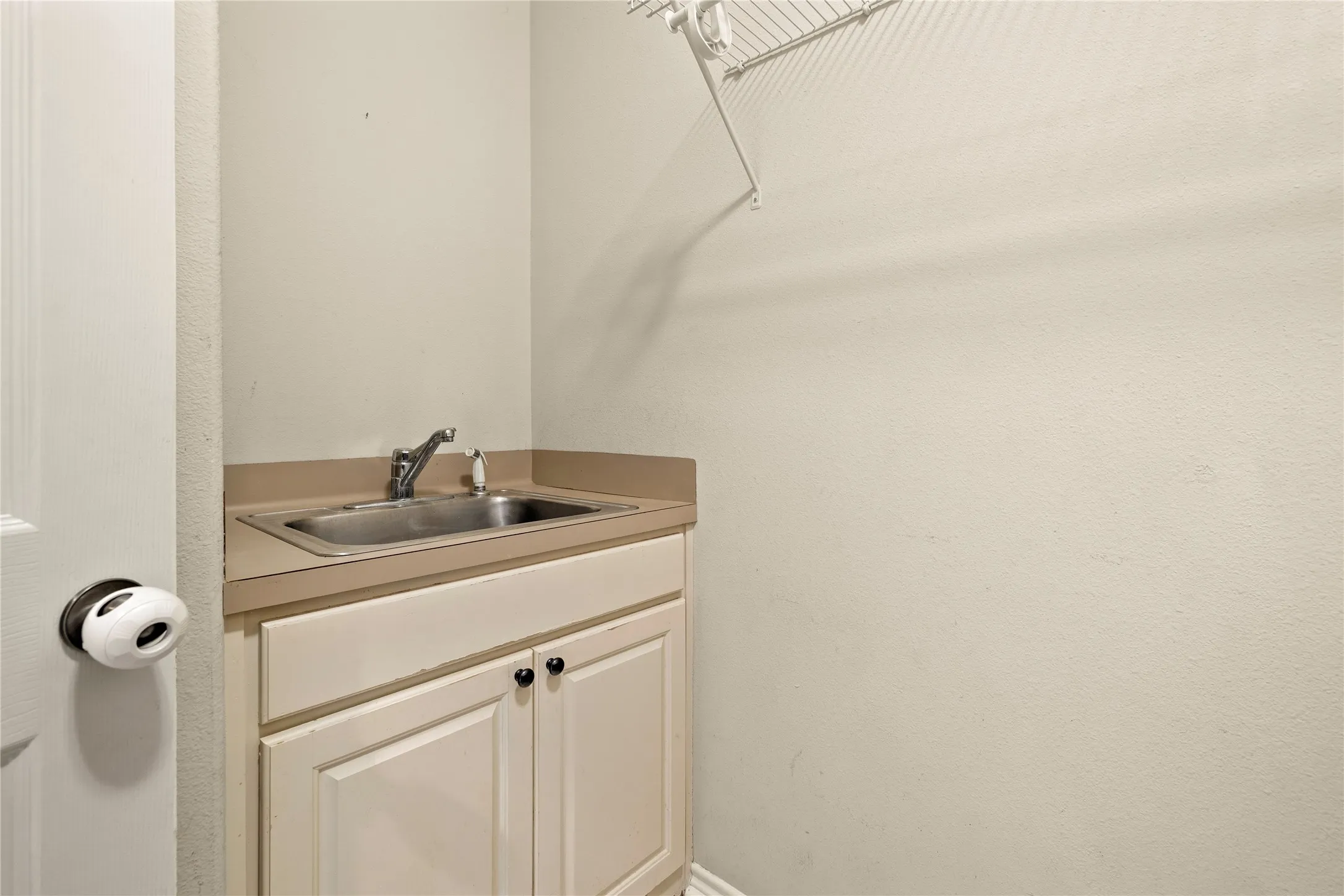 Utility sink with a chrome faucet, light-toned countertop, and white cabinetry