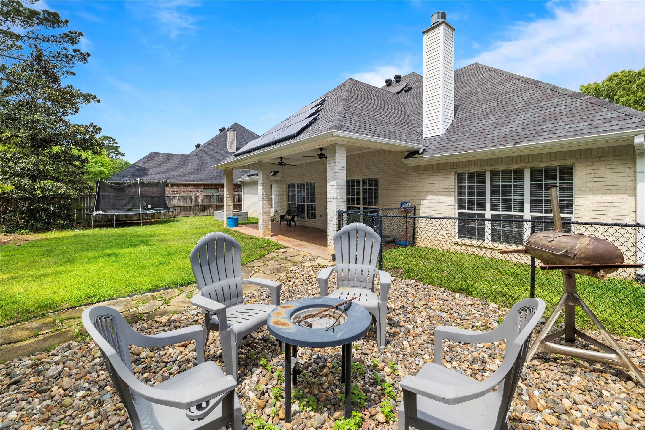 Expansive backyard featuring a stone patio, fire pit, covered porch with recessed lighting, and a manicured lawn