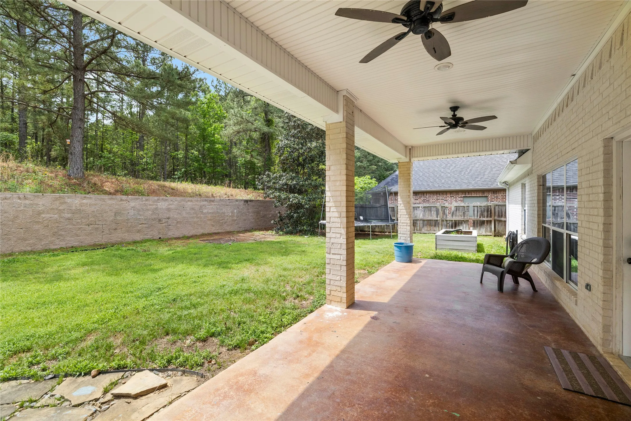 Expansive covered patio with a stained concrete floor, ceiling fans, and brick columns