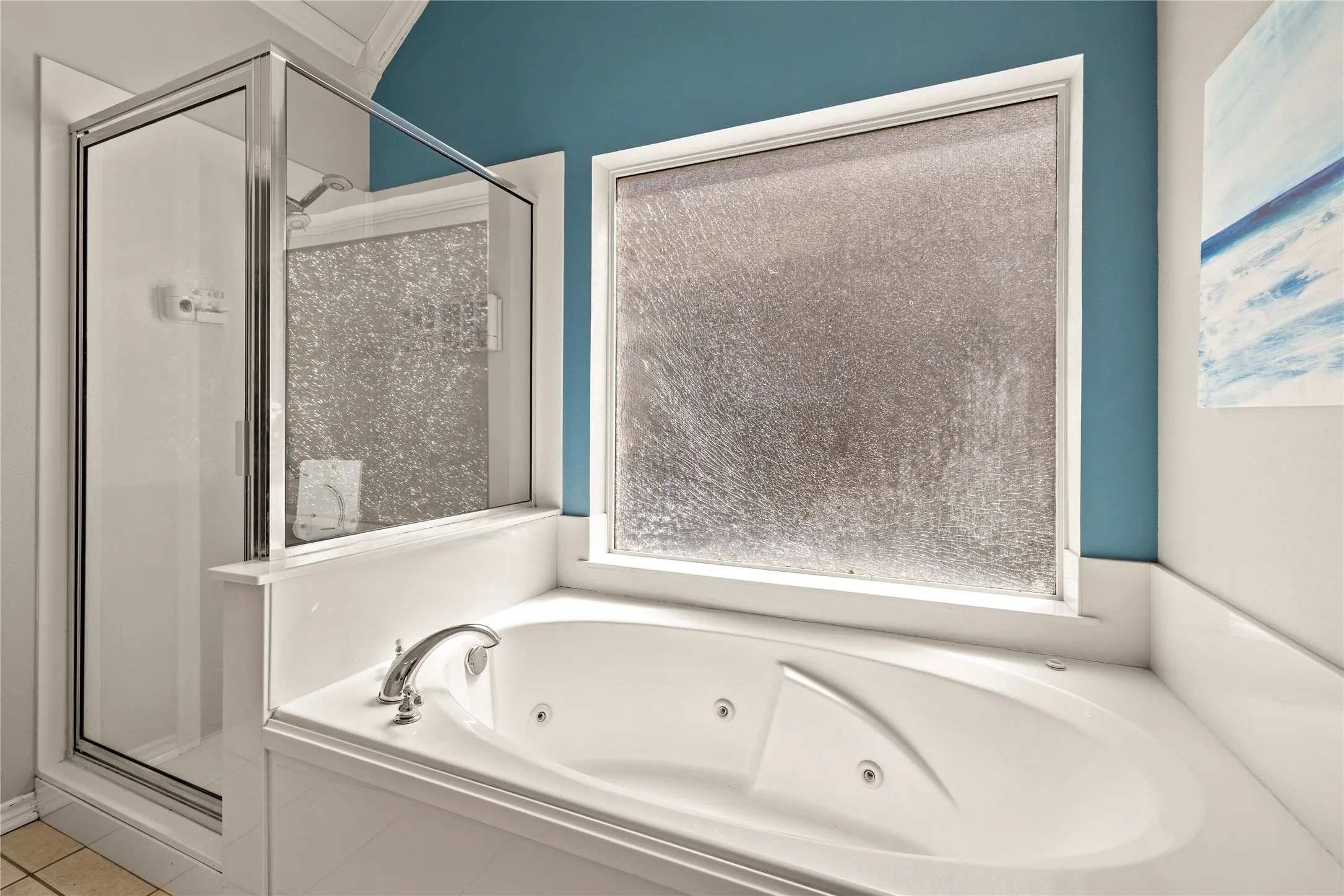 Built-in jetted tub with polished chrome fixtures, adjacent shower enclosure with glass door, and a frosted privacy window