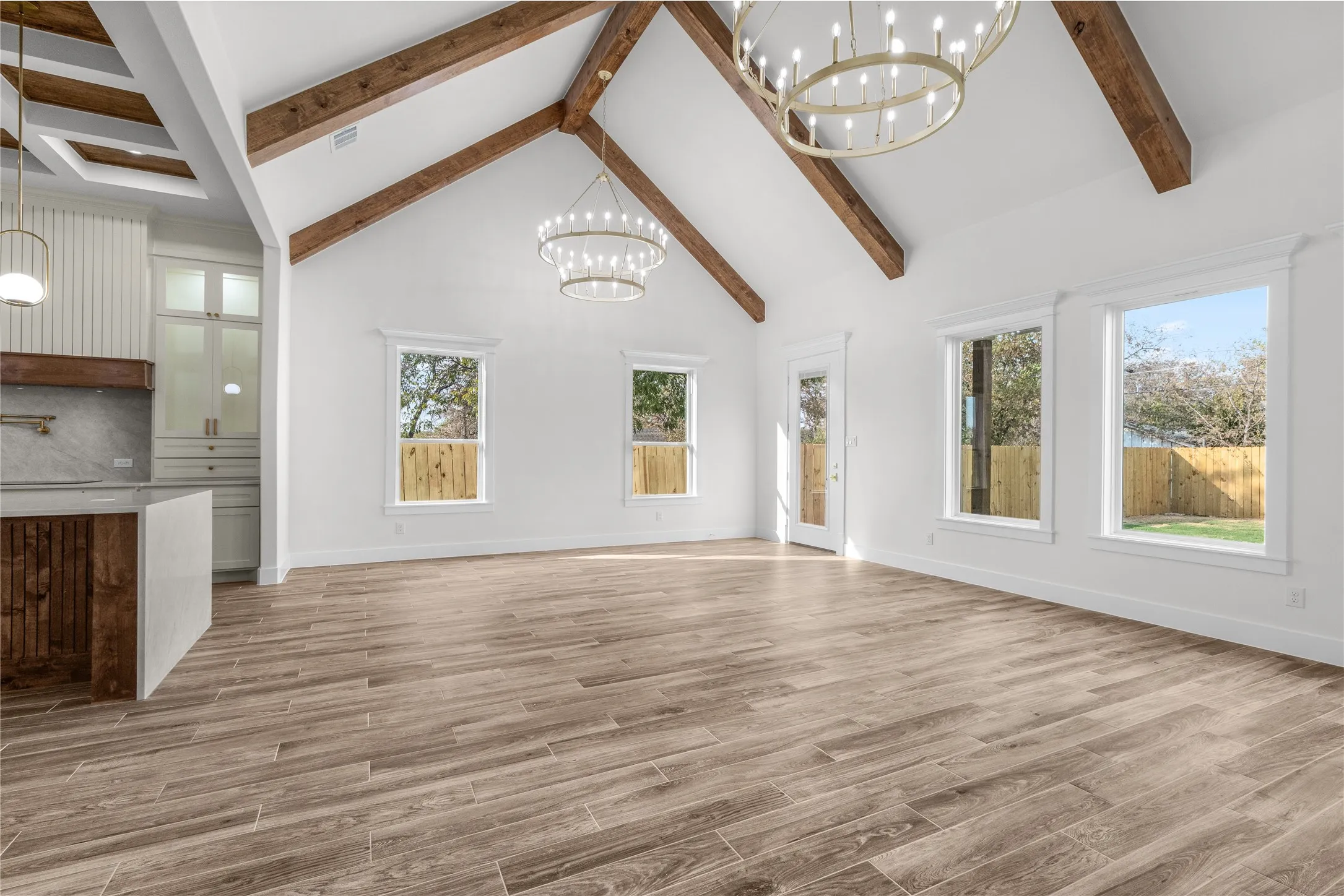 Vaulted ceiling with exposed wood beams, wood-finish flooring, multiple windows, and decorative chandelier fixtures