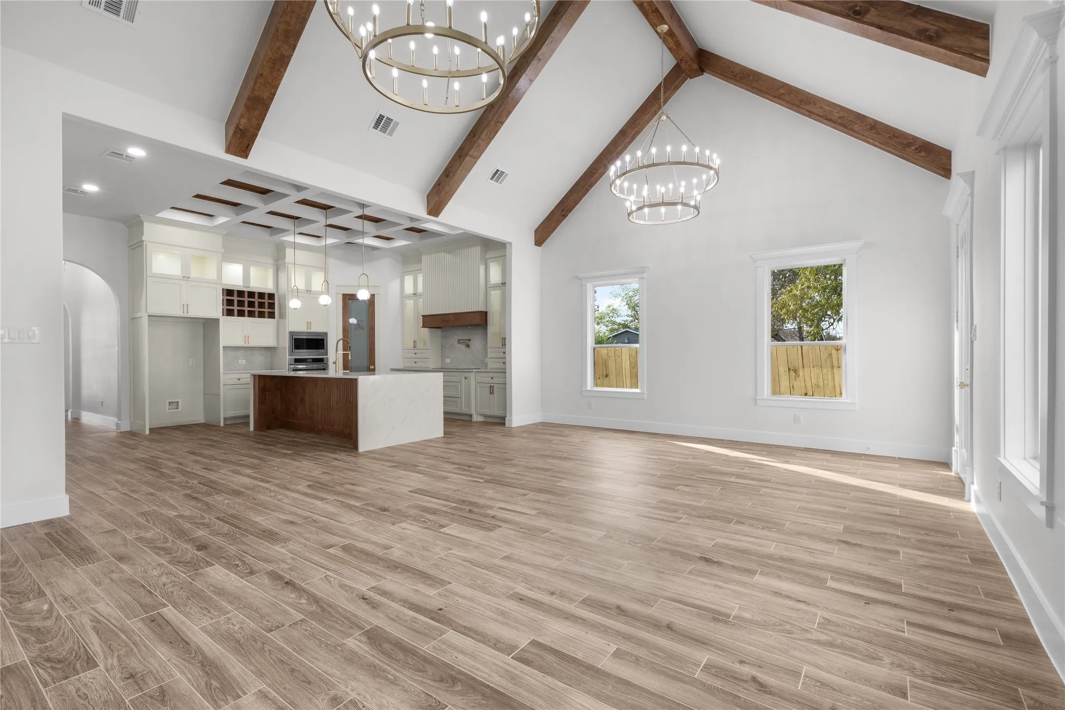 Vaulted ceiling with exposed wood beams, wood-finish flooring, recessed lighting, white cabinetry, and a kitchen island with built-in appliances