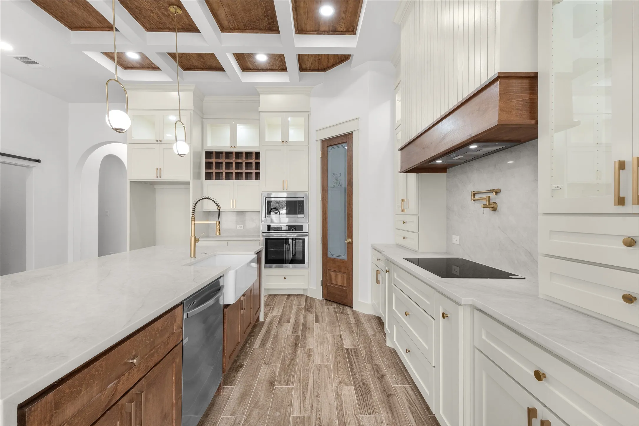 Gourmet kitchen featuring a coffered ceiling, wood-finish flooring, white cabinetry, a built-in oven, and a farmhouse sink