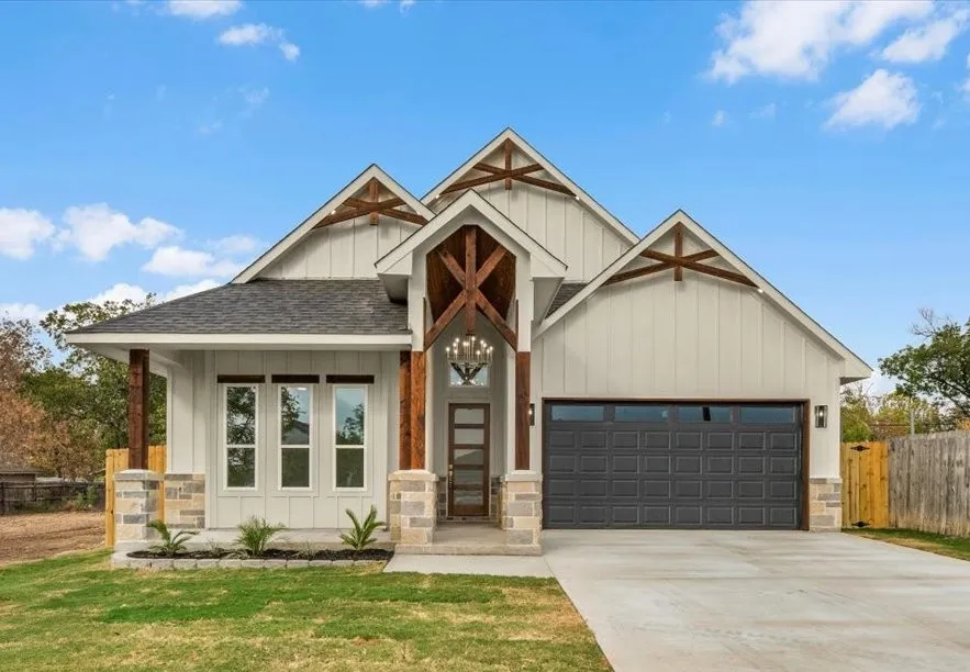 Gable rooflines featuring exposed wood beams, board and batten siding, mixed stone veneer accents, an attached two-car garage, and a covered entry with chandelier lighting