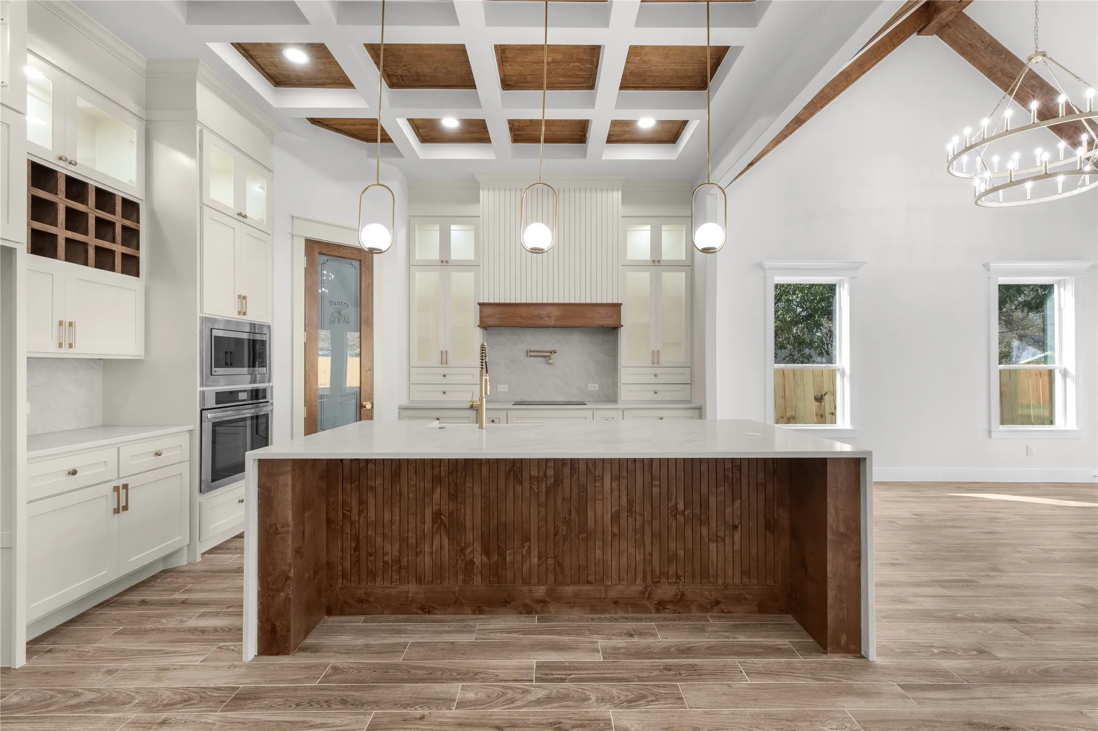 Kitchen featuring a large central island with a waterfall countertop, white cabinetry with gold-tone hardware, built-in double ovens, and a wine storage rack
