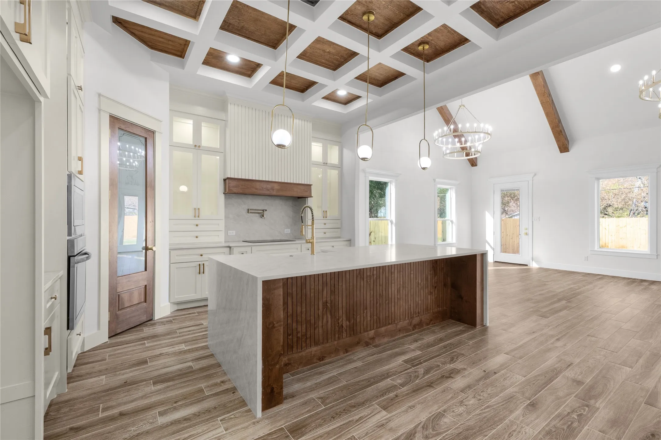 Coffered ceiling with wood-finish inserts, wood-finish flooring, kitchen island with waterfall countertop, integrated oven, and custom cabinetry