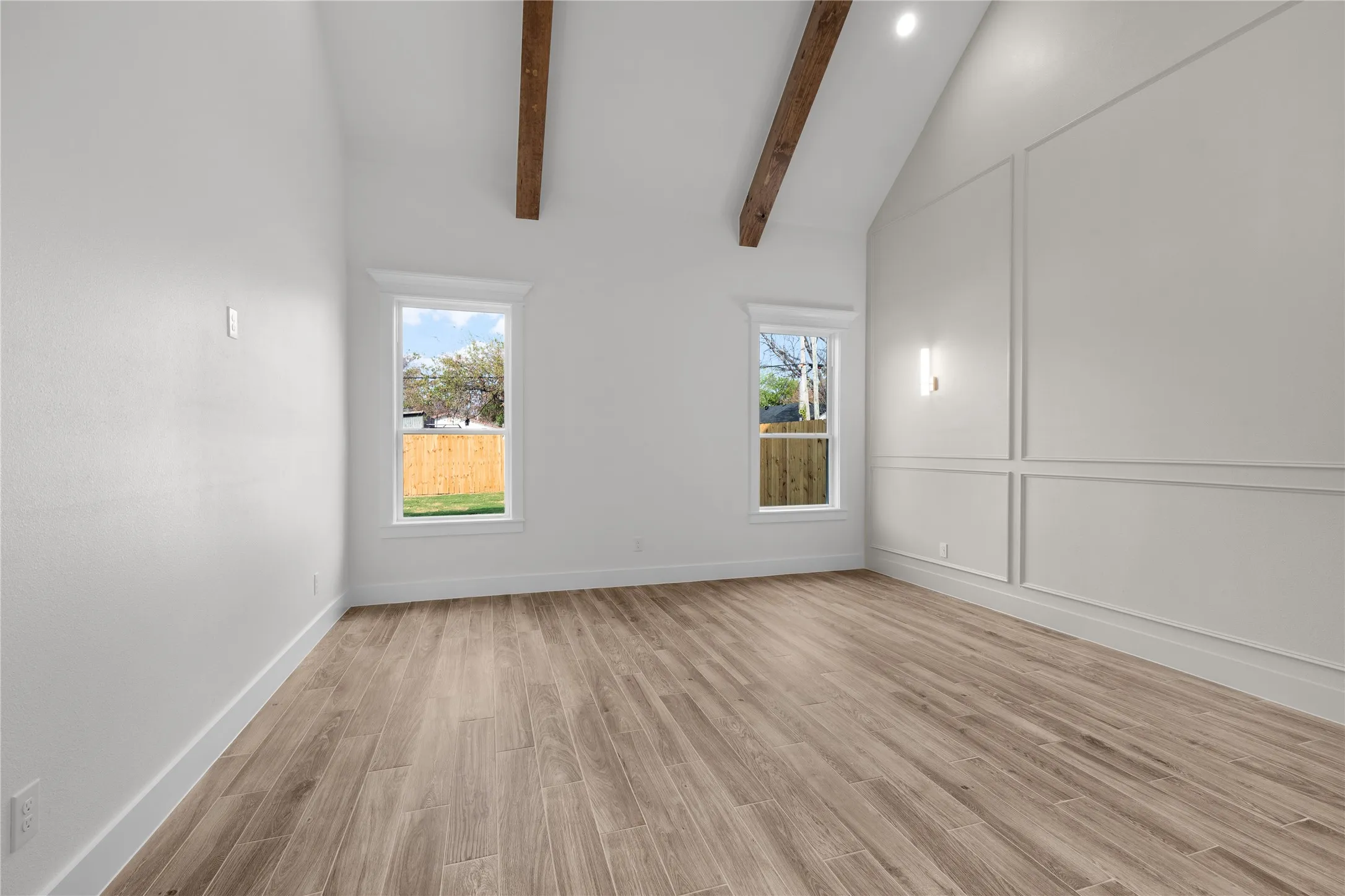 Vaulted ceiling with exposed wood beams, wood-finish flooring, two windows, wall paneling, and recessed lighting
