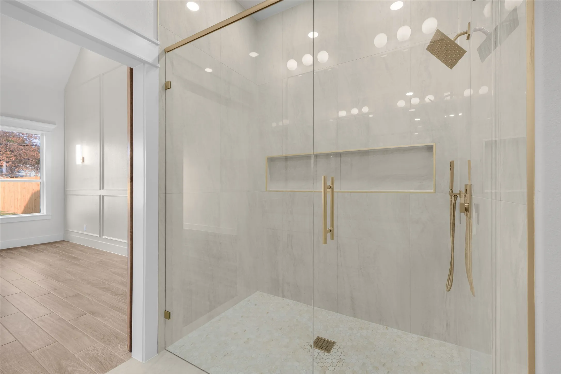 Glass-enclosed shower with gold-tone fixtures, tiled walls, and a mosaic floor
