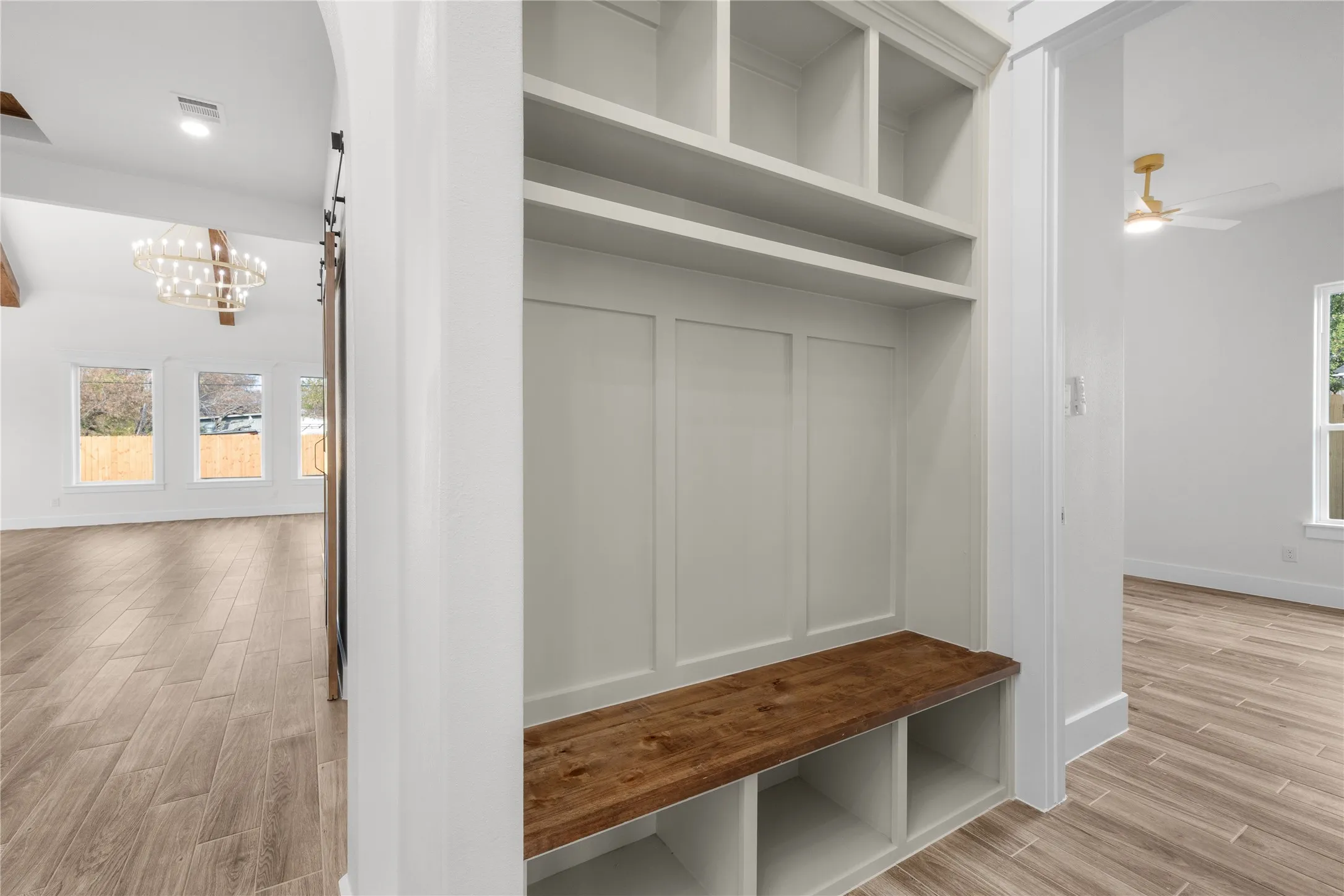 Built-in storage bench with wood-finish top, white cabinetry, wood-look flooring, and a contemporary chandelier