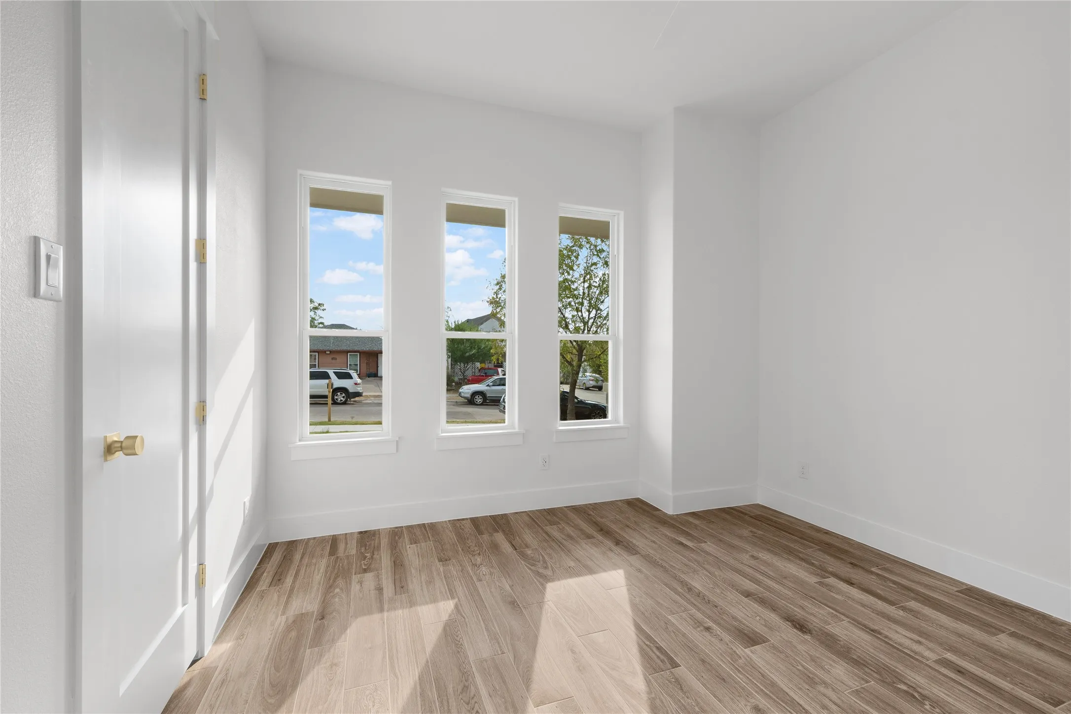 Wood-finish flooring, white walls, and three vertical windows