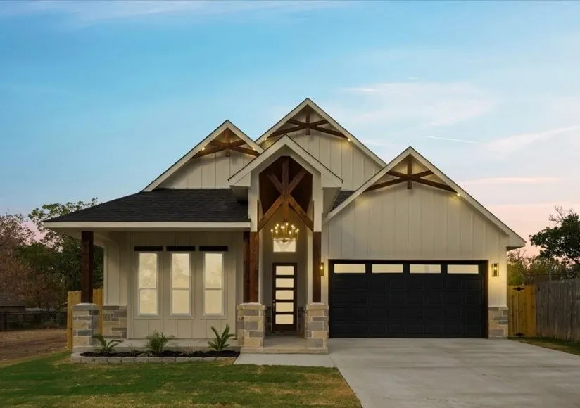 Modern farmhouse exterior with board and batten siding, stone accents, exposed wood beam details, and a dark asphalt shingle roof