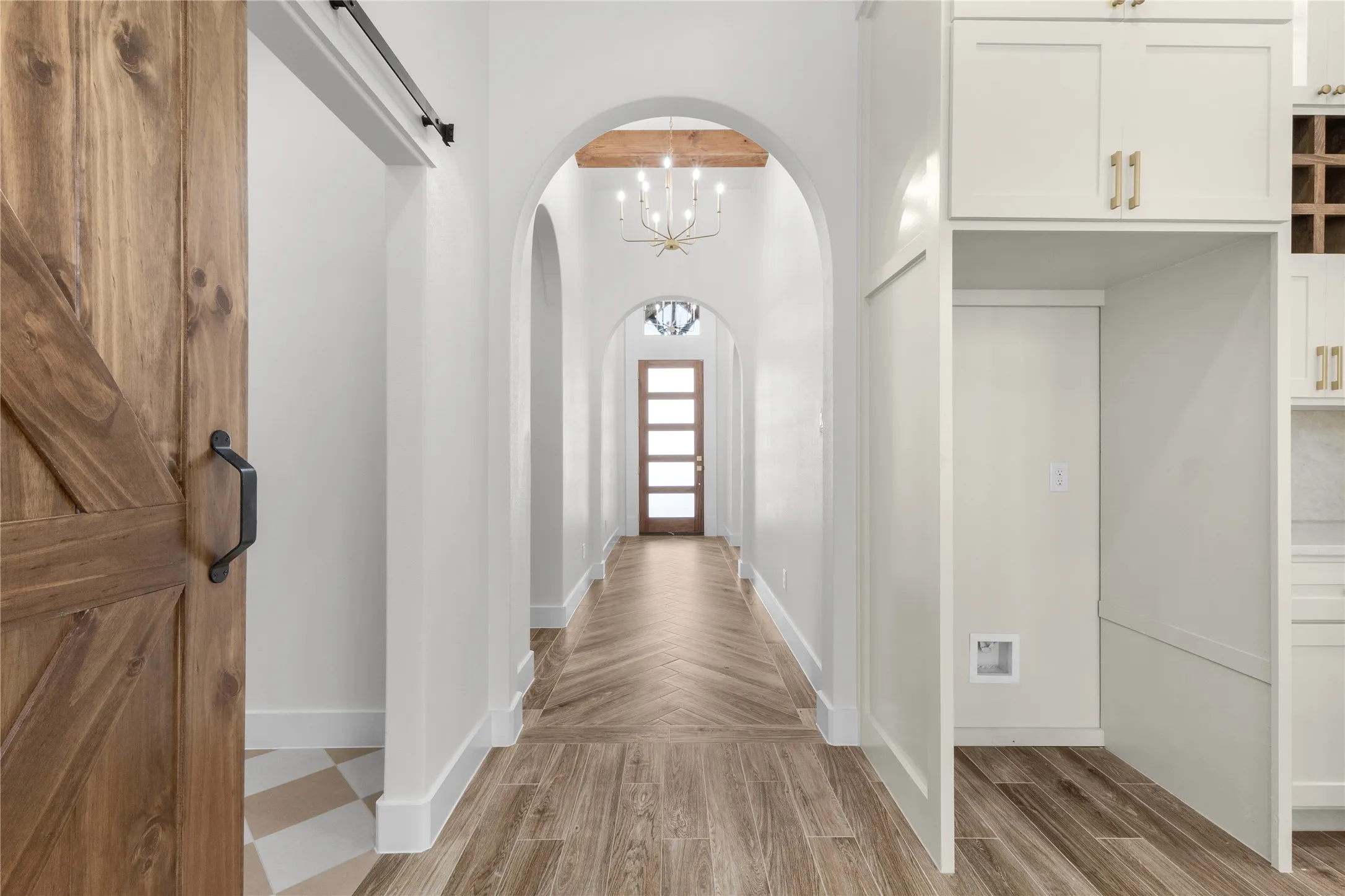 Arched doorways, wood-finish flooring in a herringbone pattern, and a natural wood barn door with black hardware
