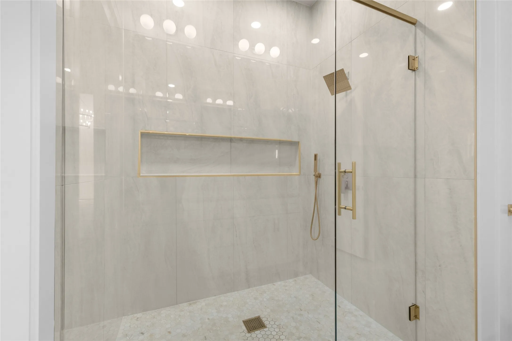 Frameless glass shower enclosure featuring a rain shower head, hand-held shower, integrated wall niche, and mosaic tile flooring