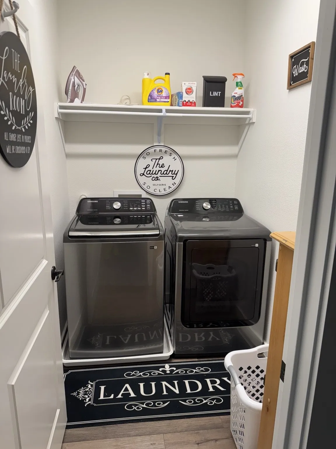 Integrated laundry area featuring wood-finish flooring, a white wall-mounted shelf, and light-toned walls