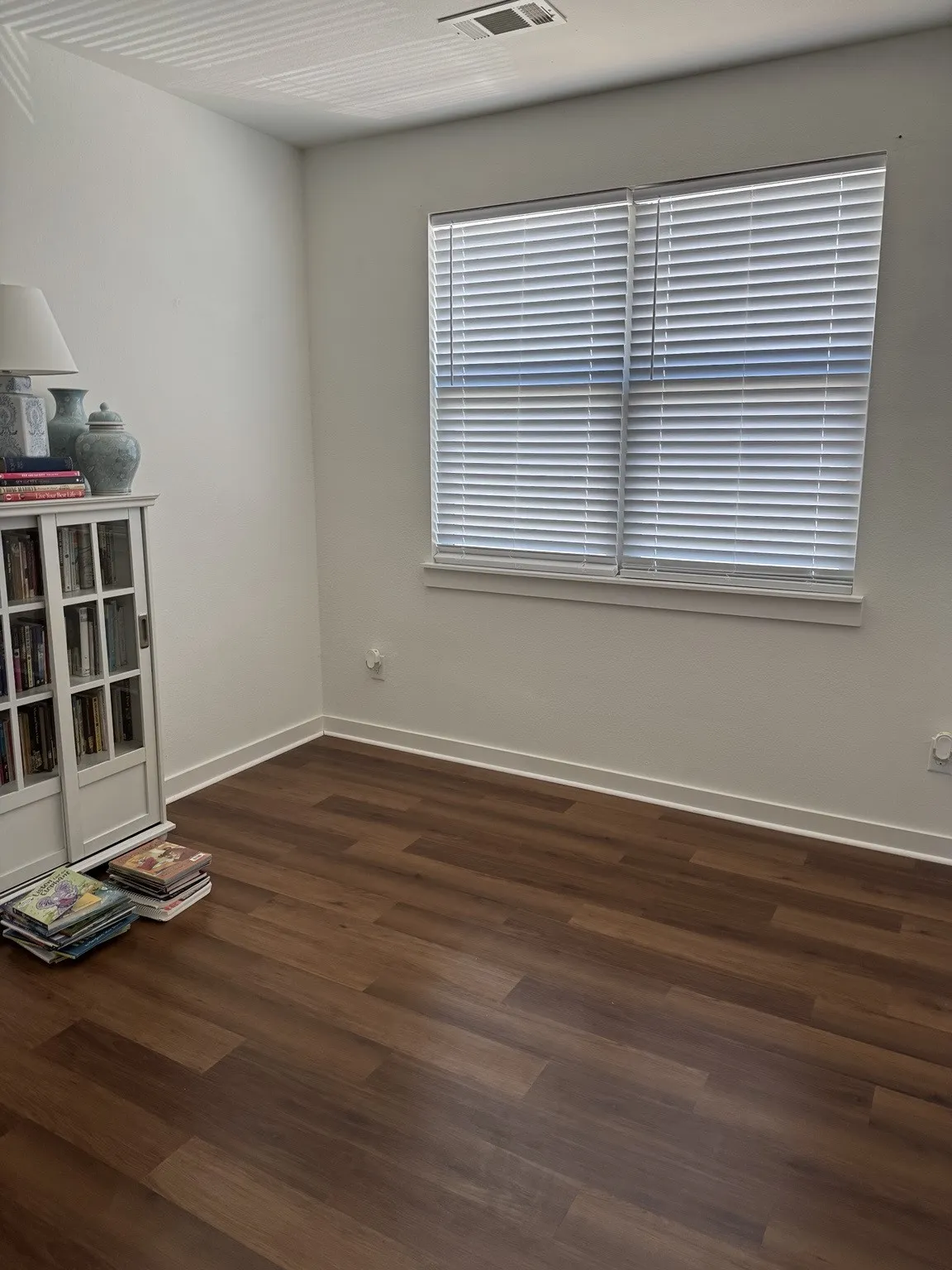 Wood-finish flooring, white walls, and a window with blinds