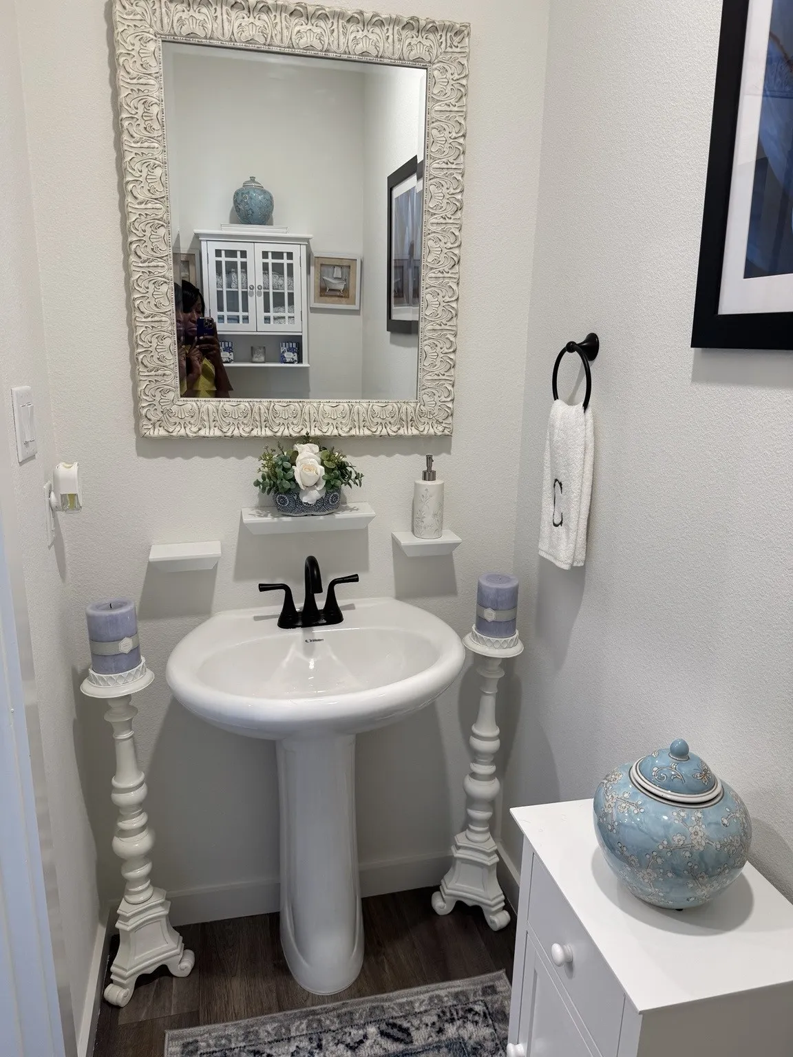 Pedestal sink with a matte black faucet, wall-mounted mirror with an ornate frame, and wood-finish flooring