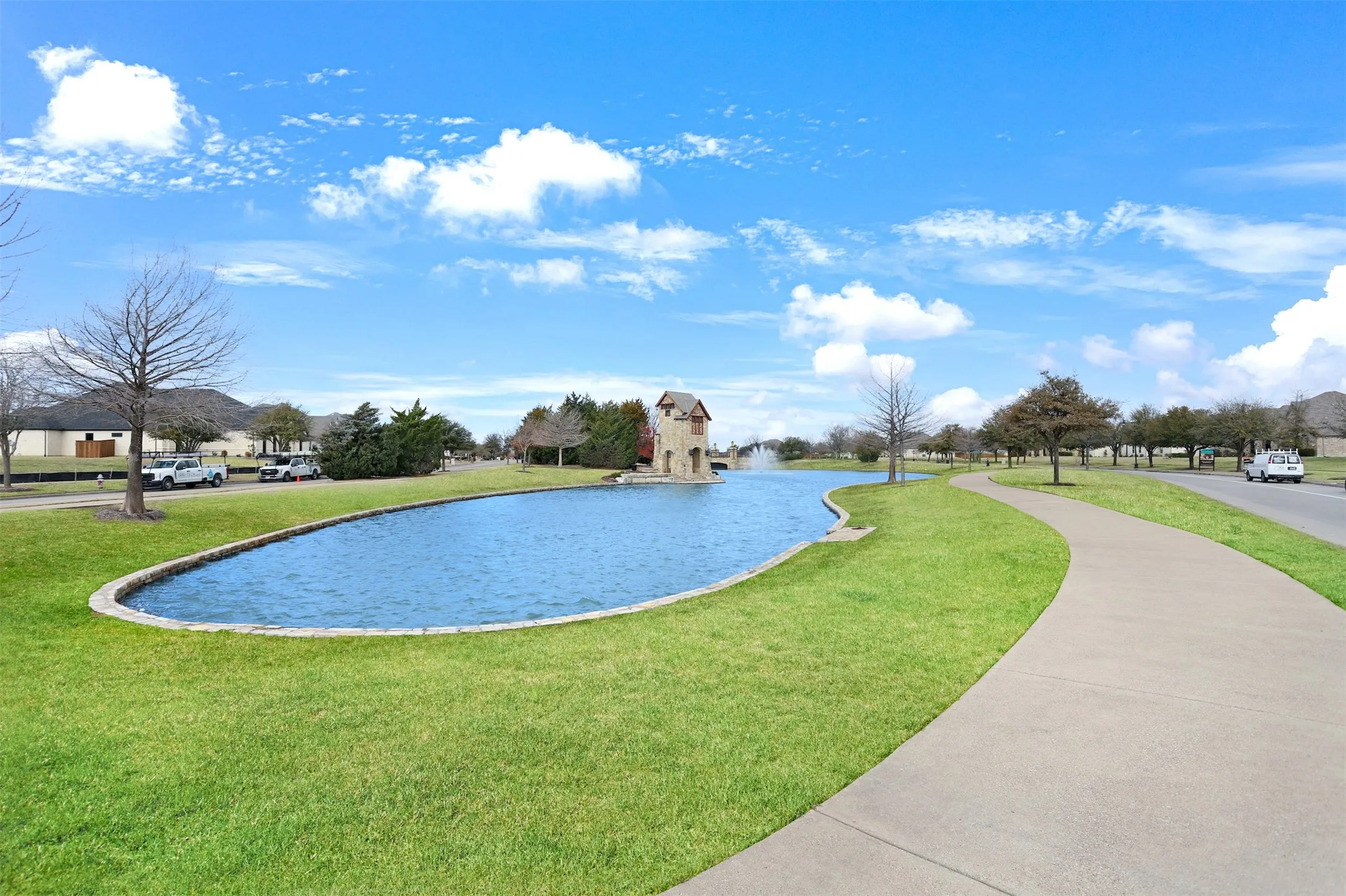 Winding concrete pathway bordering a manicured lawn and a tranquil pond