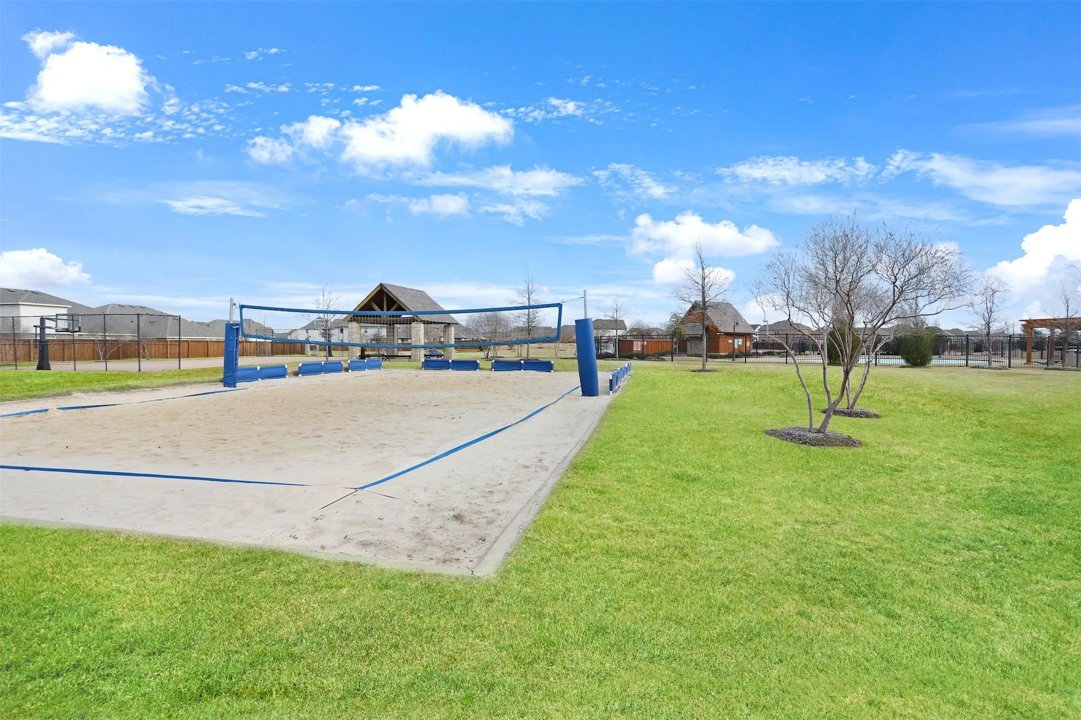 Sand volleyball court with a net, green lawn areas, and a nearby covered pavilion structure