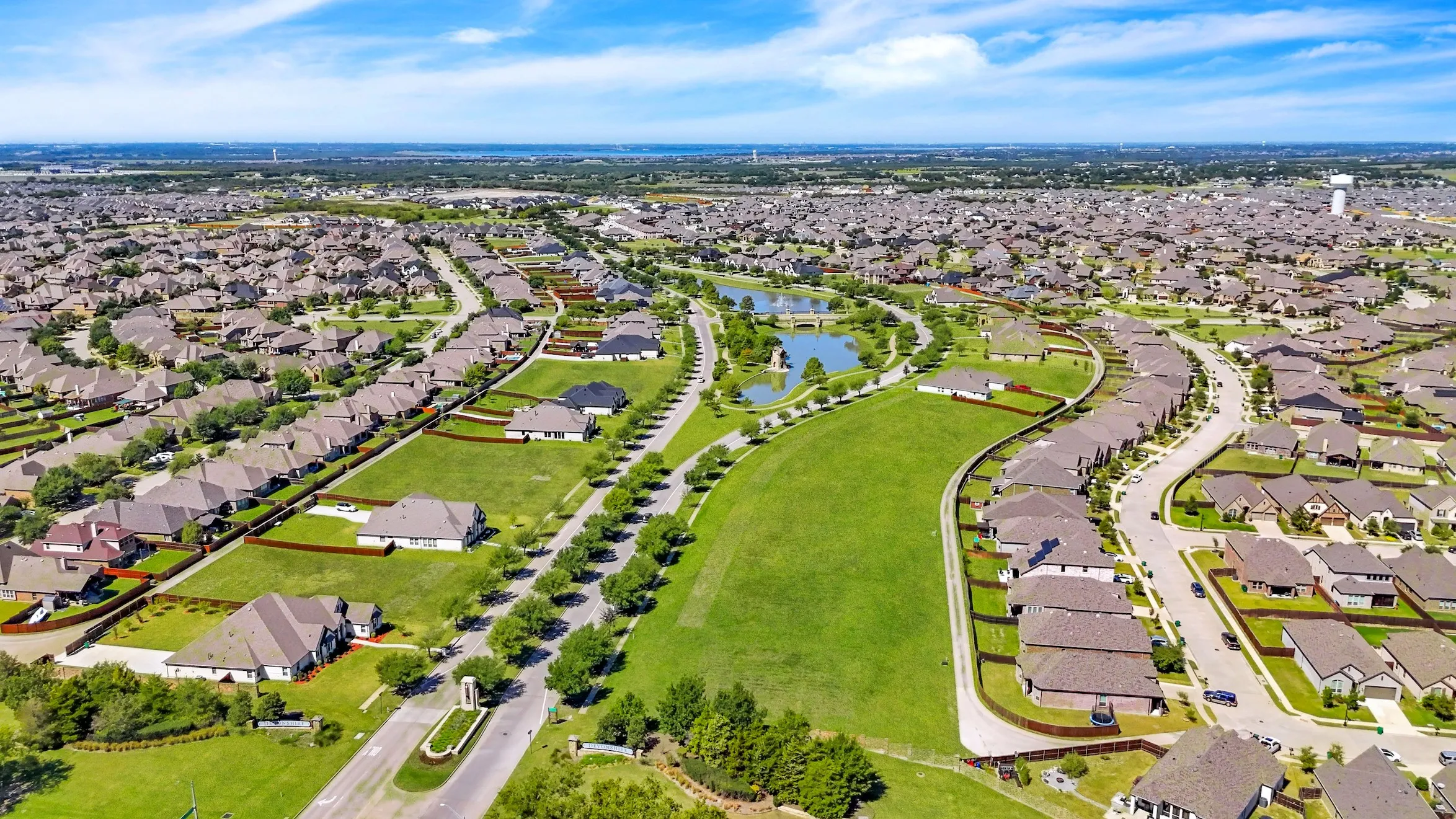 Expansive residential development featuring paved streets, mature landscaping, green spaces, and a water feature