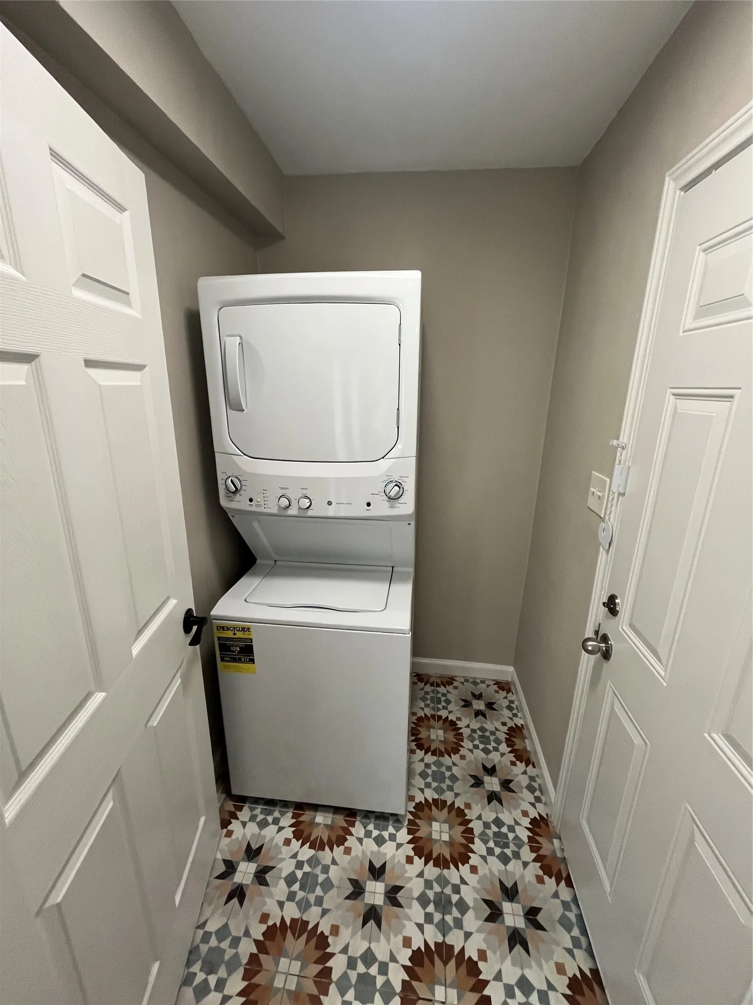Compact laundry area featuring a stacked washer and dryer, patterned floor tile, and painted walls