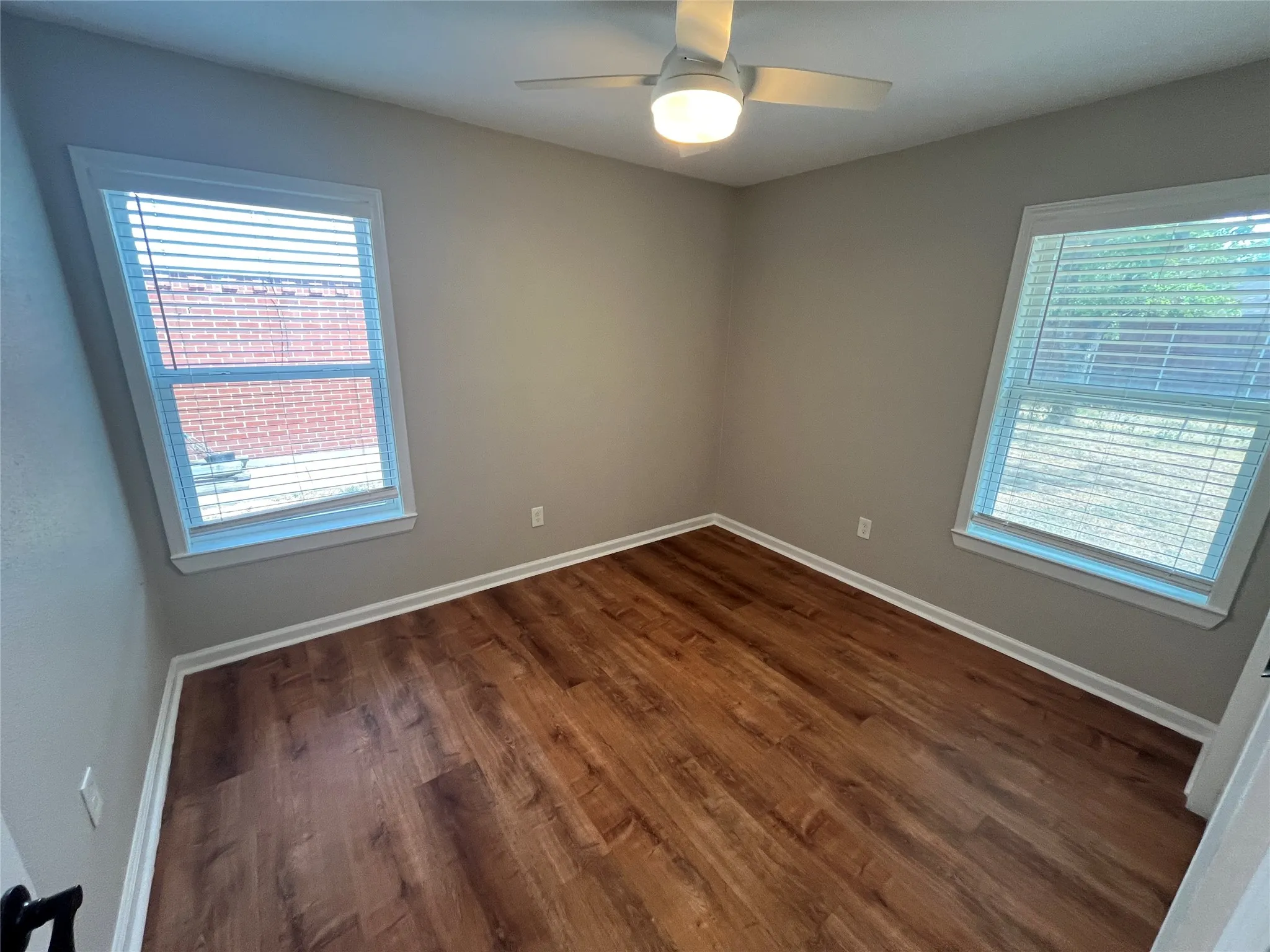 Wood-finish flooring, neutral wall tones, white trim, and a ceiling fan with integrated lighting