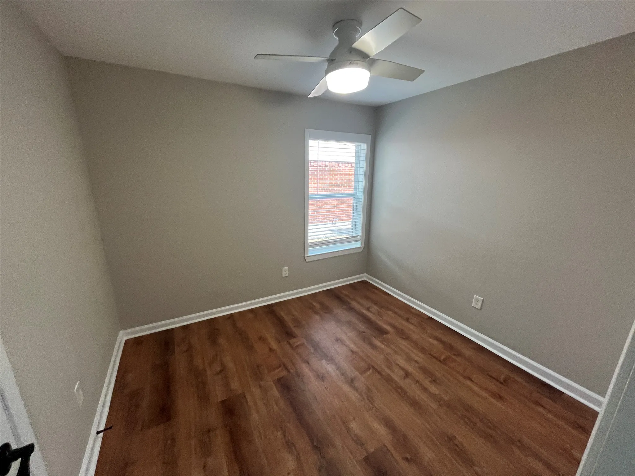 Wood-finish flooring, neutral wall tones, white trim, ceiling fan with integrated lighting, and window with blinds