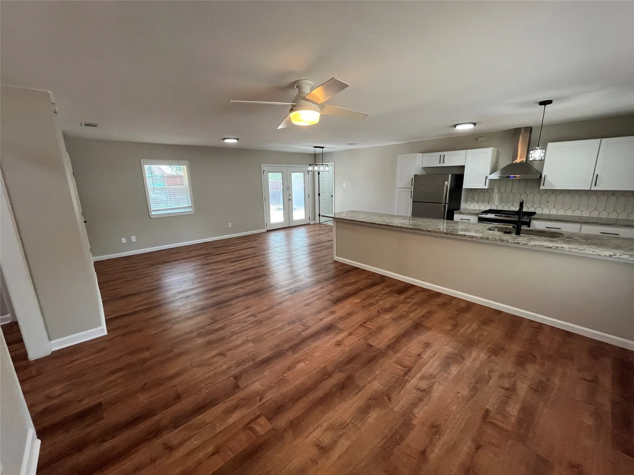 Open-concept living space with wood-finish flooring, a contemporary kitchen with light-toned cabinetry, and a spacious island featuring a stone countertop