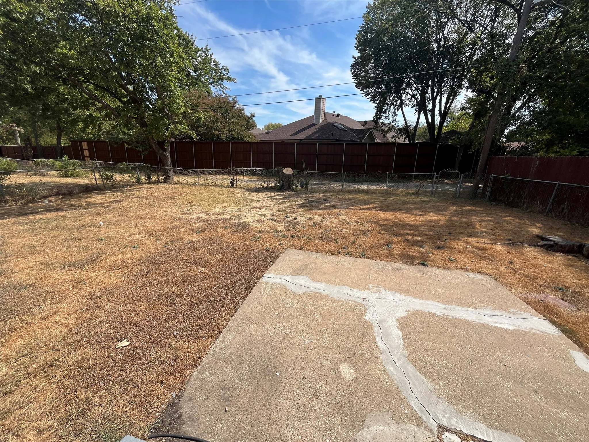Expansive backyard featuring a concrete patio, chain-link fencing, and mature trees