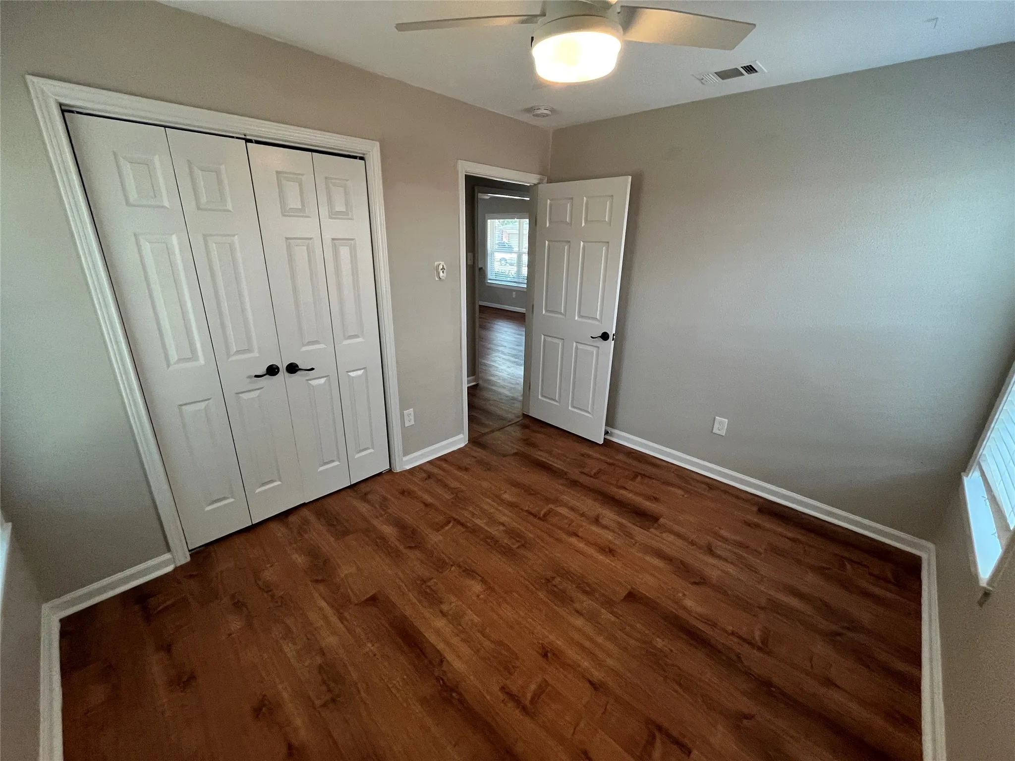 Wood-finish flooring with white trim, a ceiling fan with integrated lighting, and a white paneled door