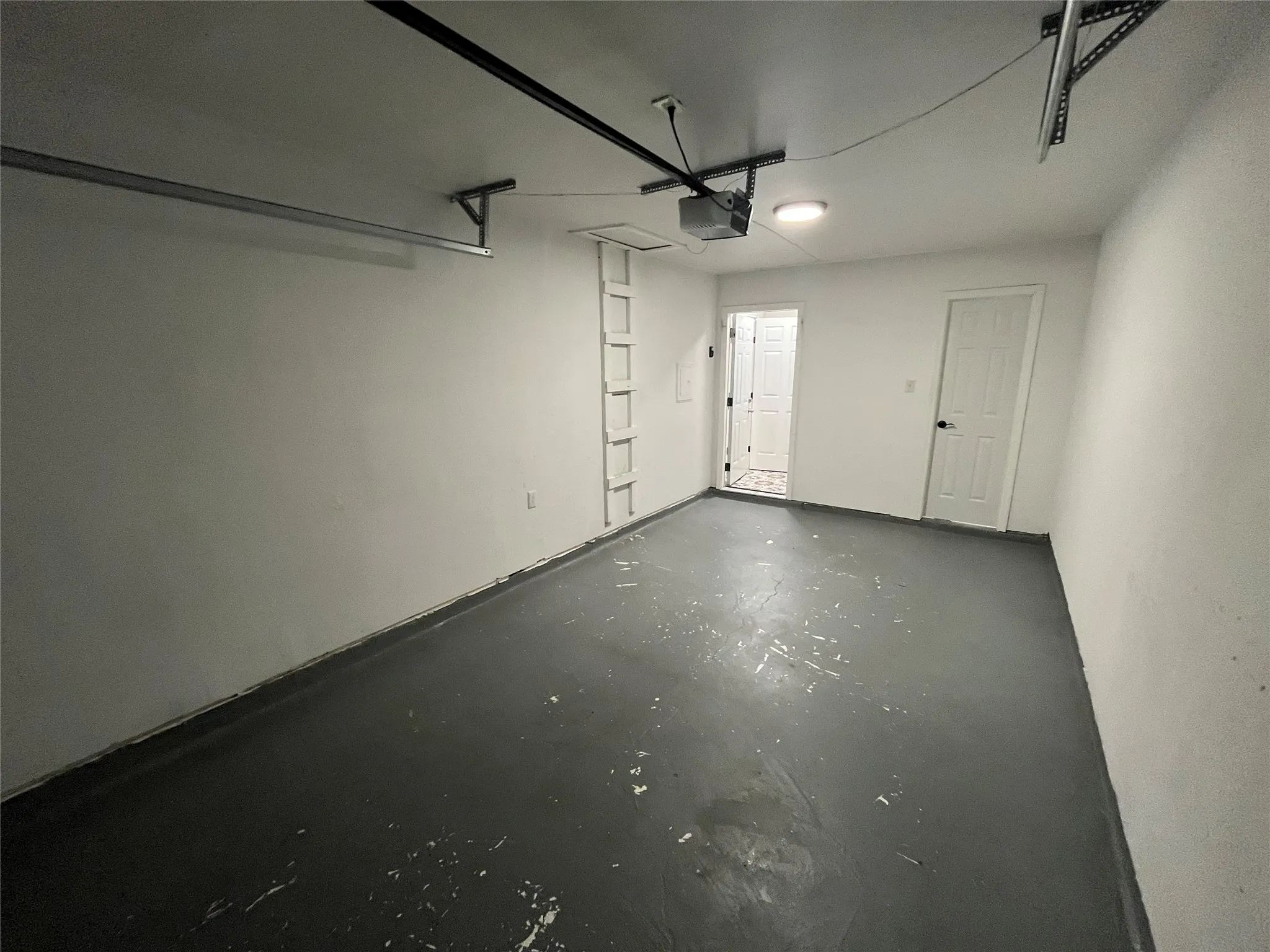 Attached garage with painted concrete flooring, overhead garage door rails, and a built-in access ladder