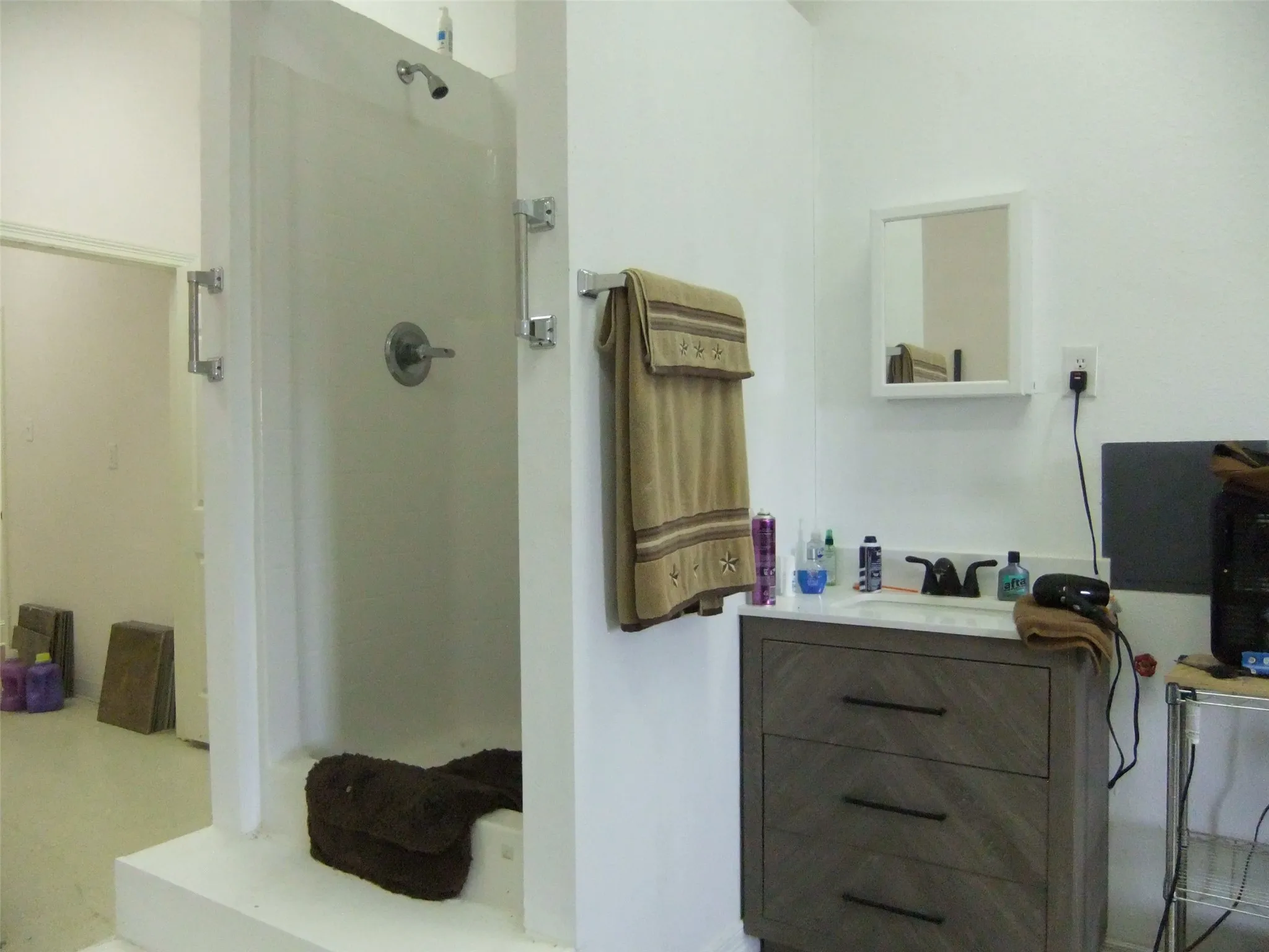 Full bathroom behind sanctuary Walk-in shower with chrome fixtures, single vanity with a light wood-finish cabinet, stone-finish countertop, and wall-mounted mirror
