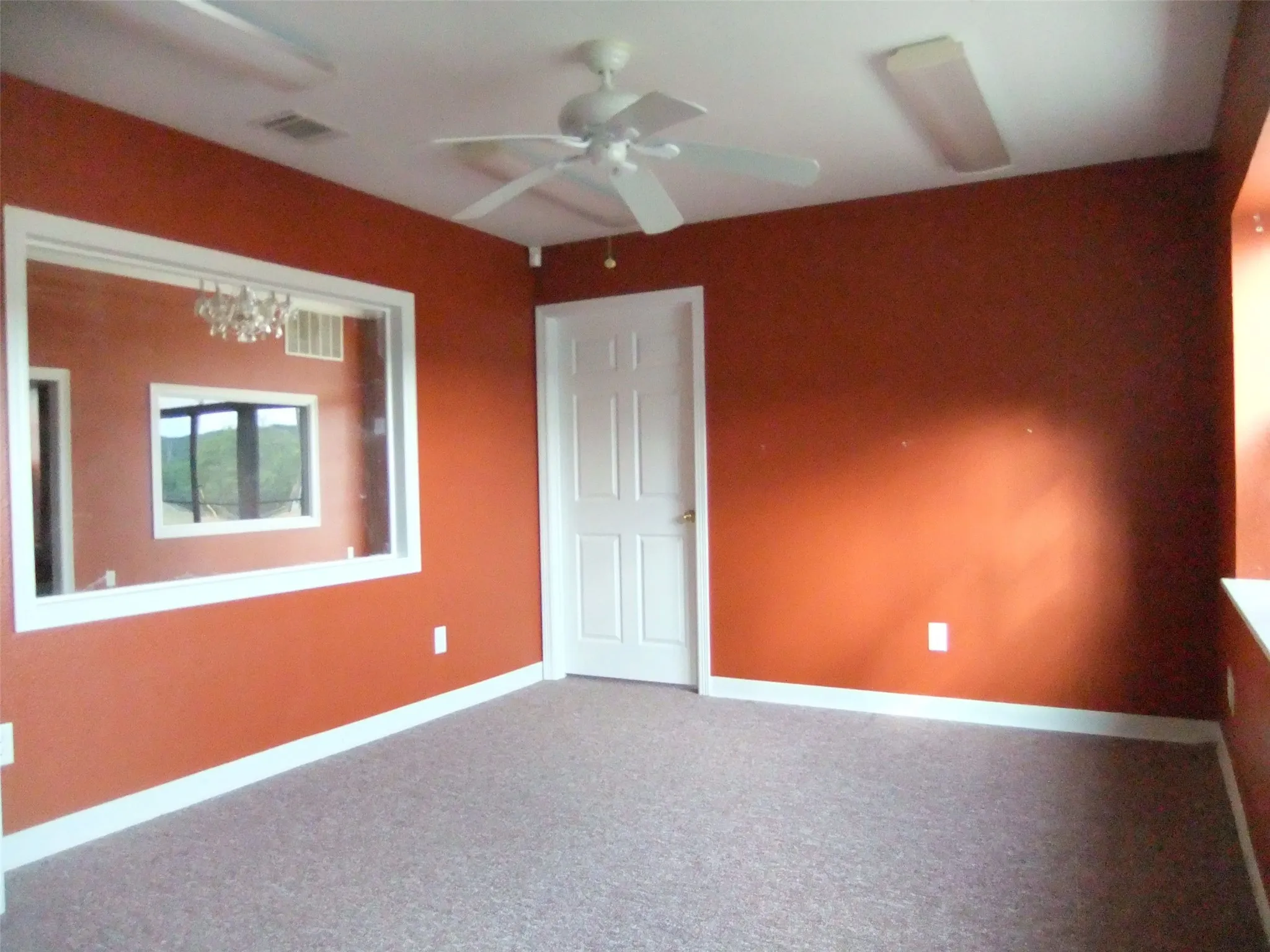 Spacious room featuring warm burnt-orange walls with crisp white trim, recessed ceiling lighting with ceiling fan, plush carpet flooring, and dual white six-panel doors