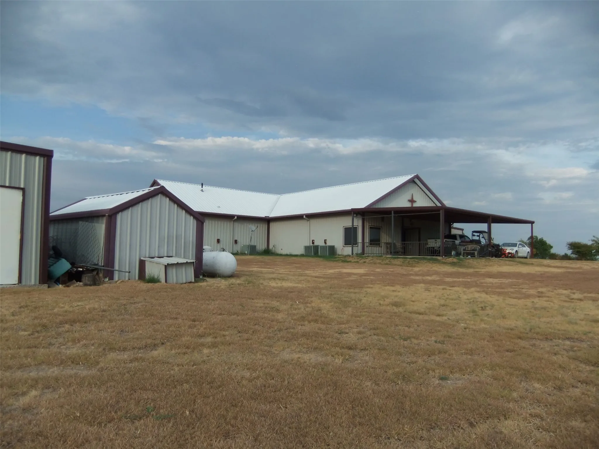 Metal construction with a white roof, covered porch, and detached shed