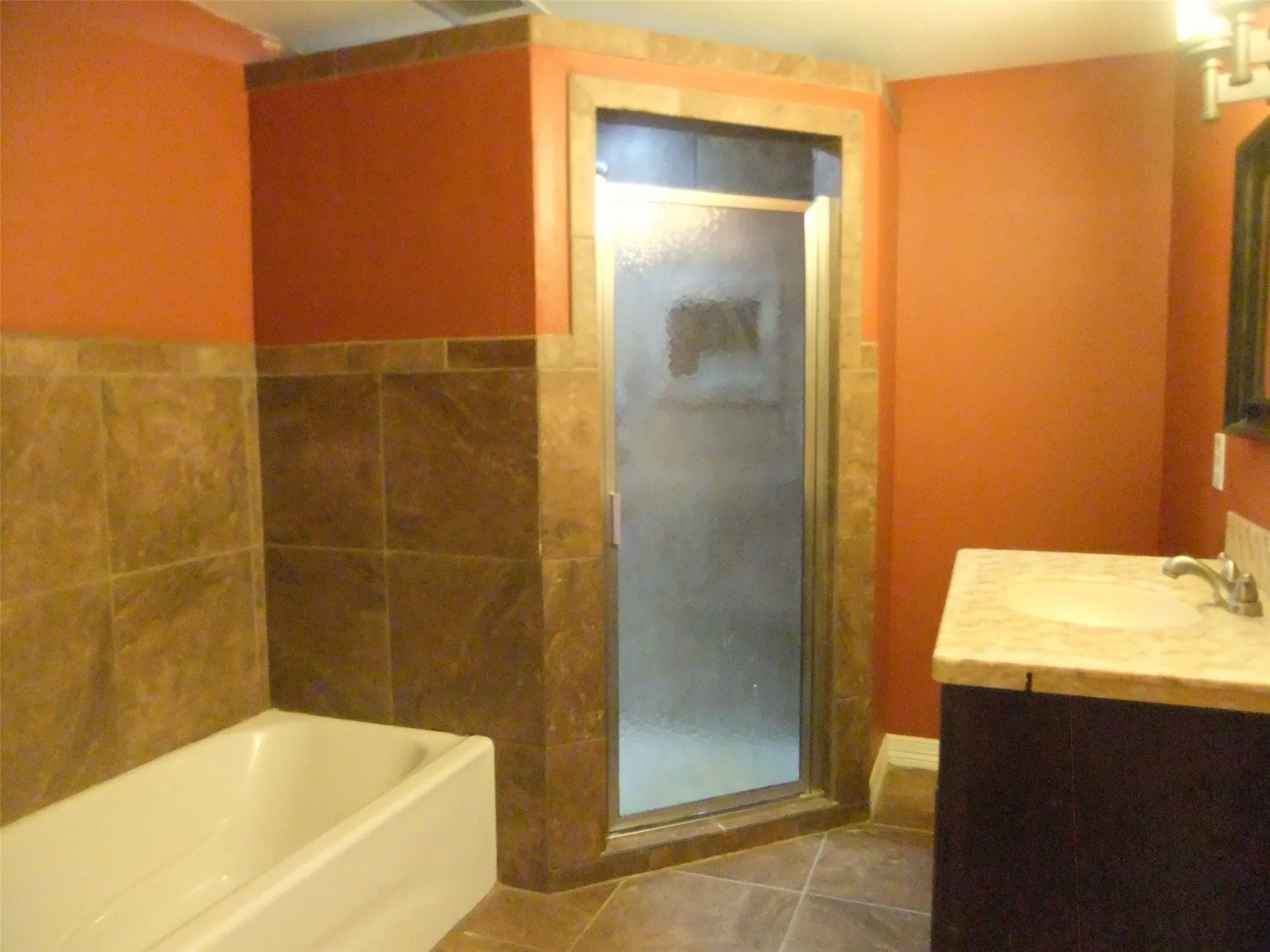 Second apartment Built-in bathtub, floor-to-ceiling tile, corner shower with glass enclosure, dark wood-finish vanity, and integrated sink with light-colored countertop