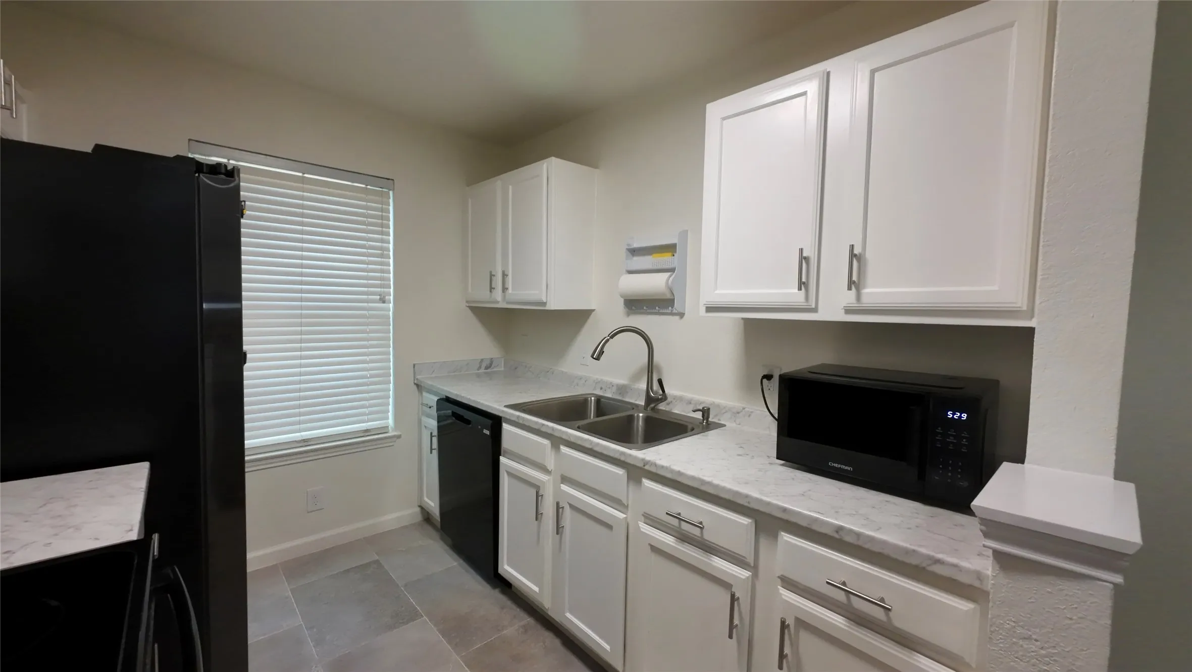 Kitchen with white cabinetry, light countertops, stainless steel double basin sink, and tile flooring