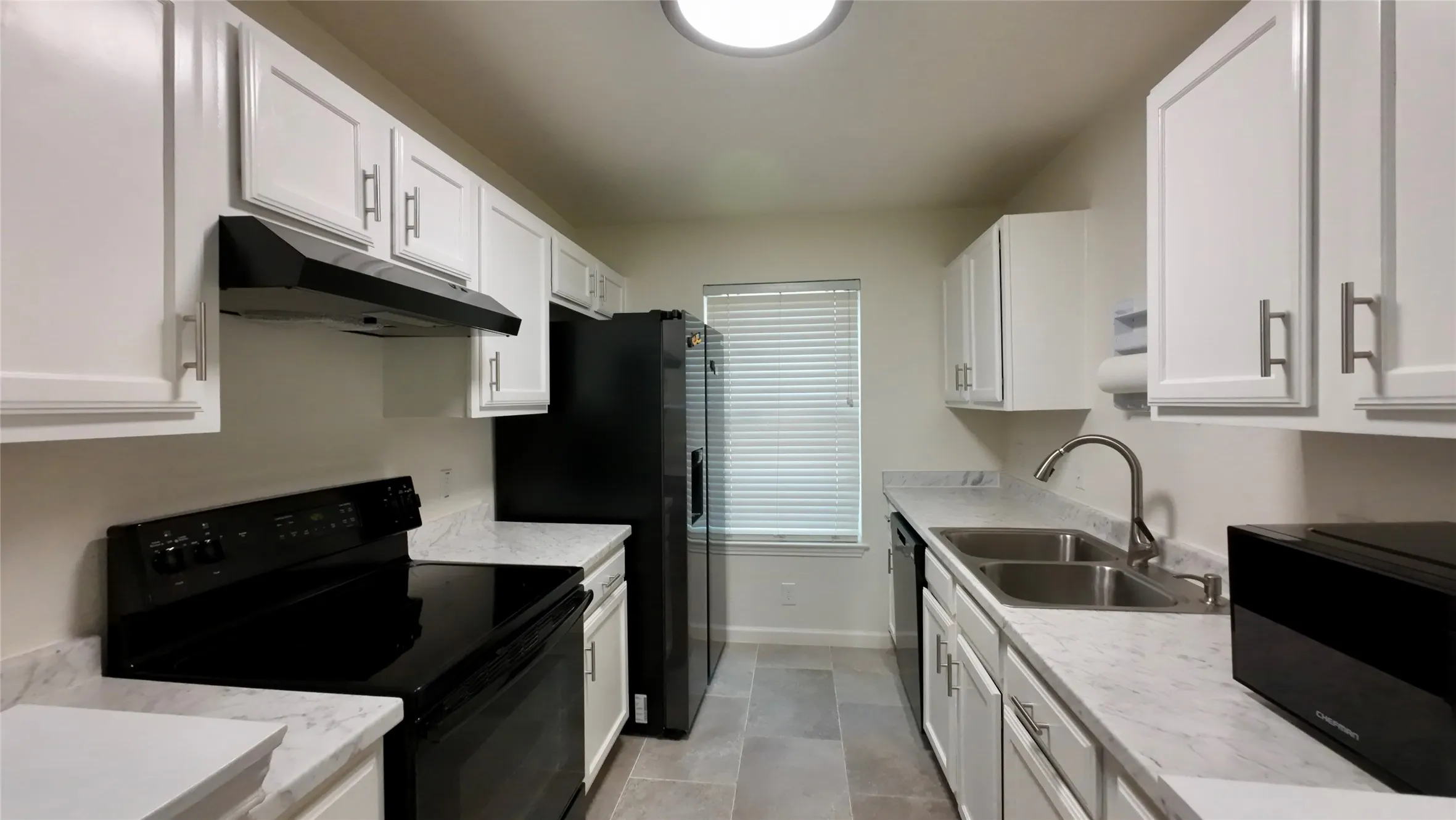 Galley kitchen featuring white cabinetry, light-toned countertops, tile flooring, and a stainless steel double-basin sink