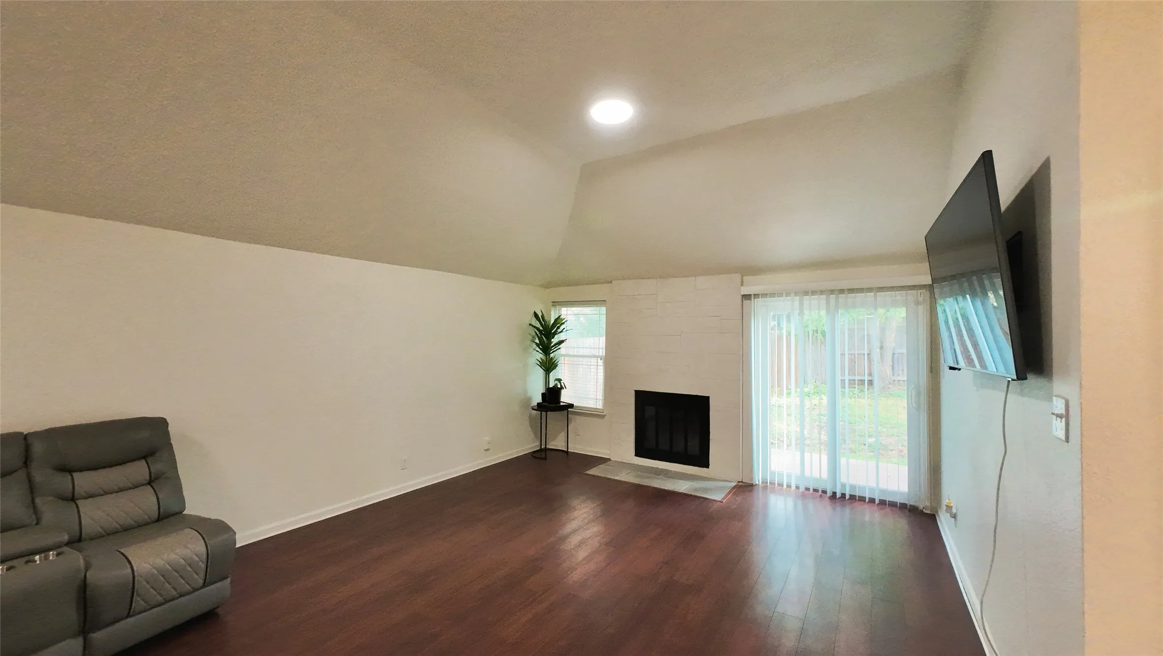 Vaulted ceiling, wood-finish flooring, brick fireplace surround, sliding glass door, recessed lighting