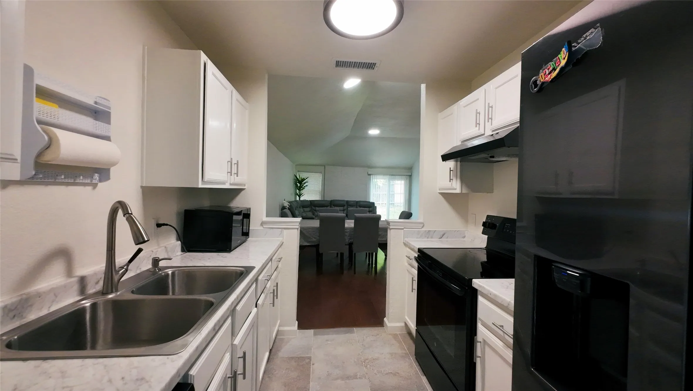 Galley kitchen featuring white cabinetry, light-toned countertops, a stainless steel double sink with a gooseneck faucet, and dark-toned appliances