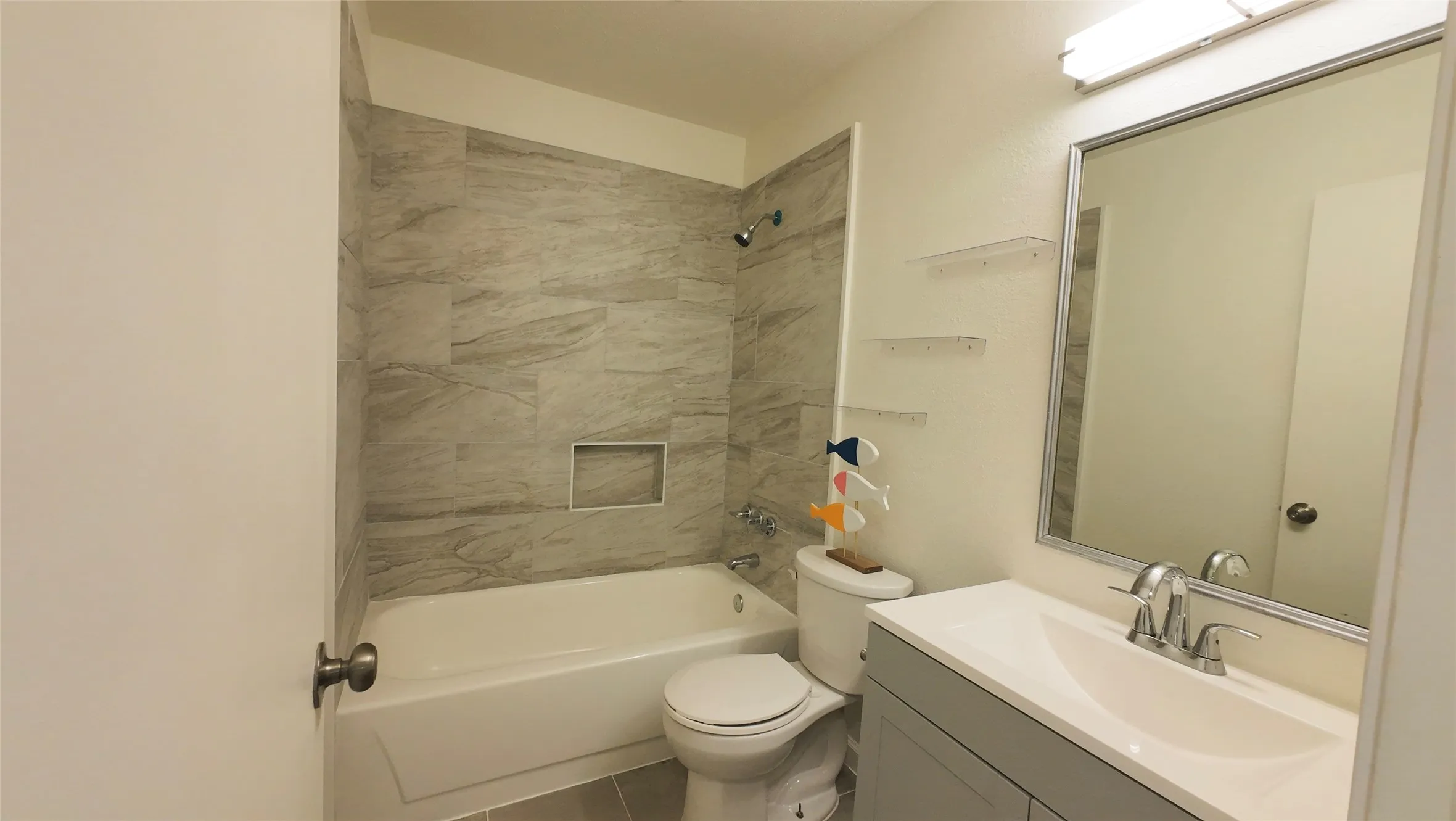 Bathroom featuring a white bathtub, gray tile surround, built-in shower niche, gray vanity with integrated sink, and a framed mirror