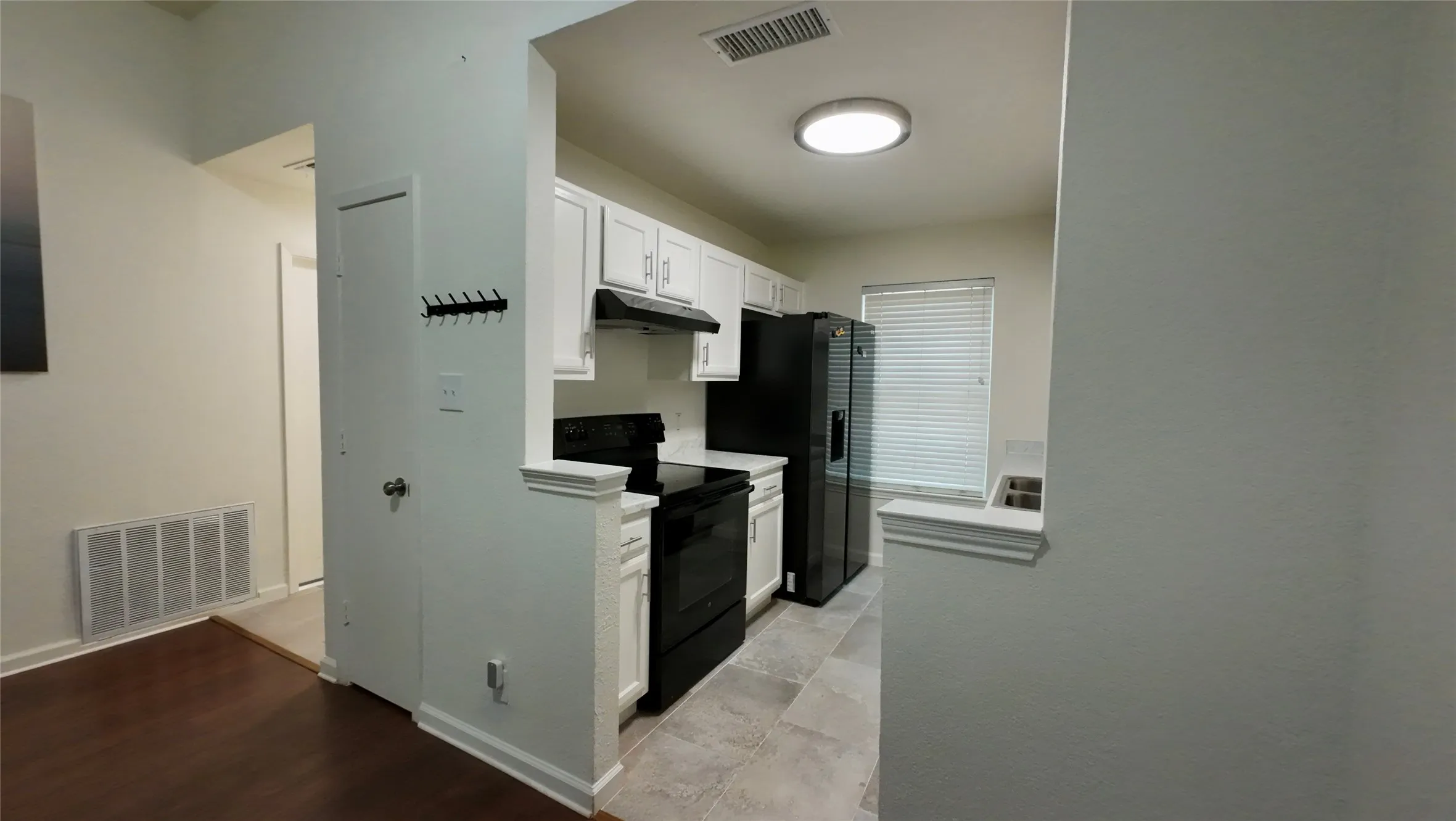 Kitchen featuring black appliances, white cabinetry, tile flooring, and a flush-mount ceiling light