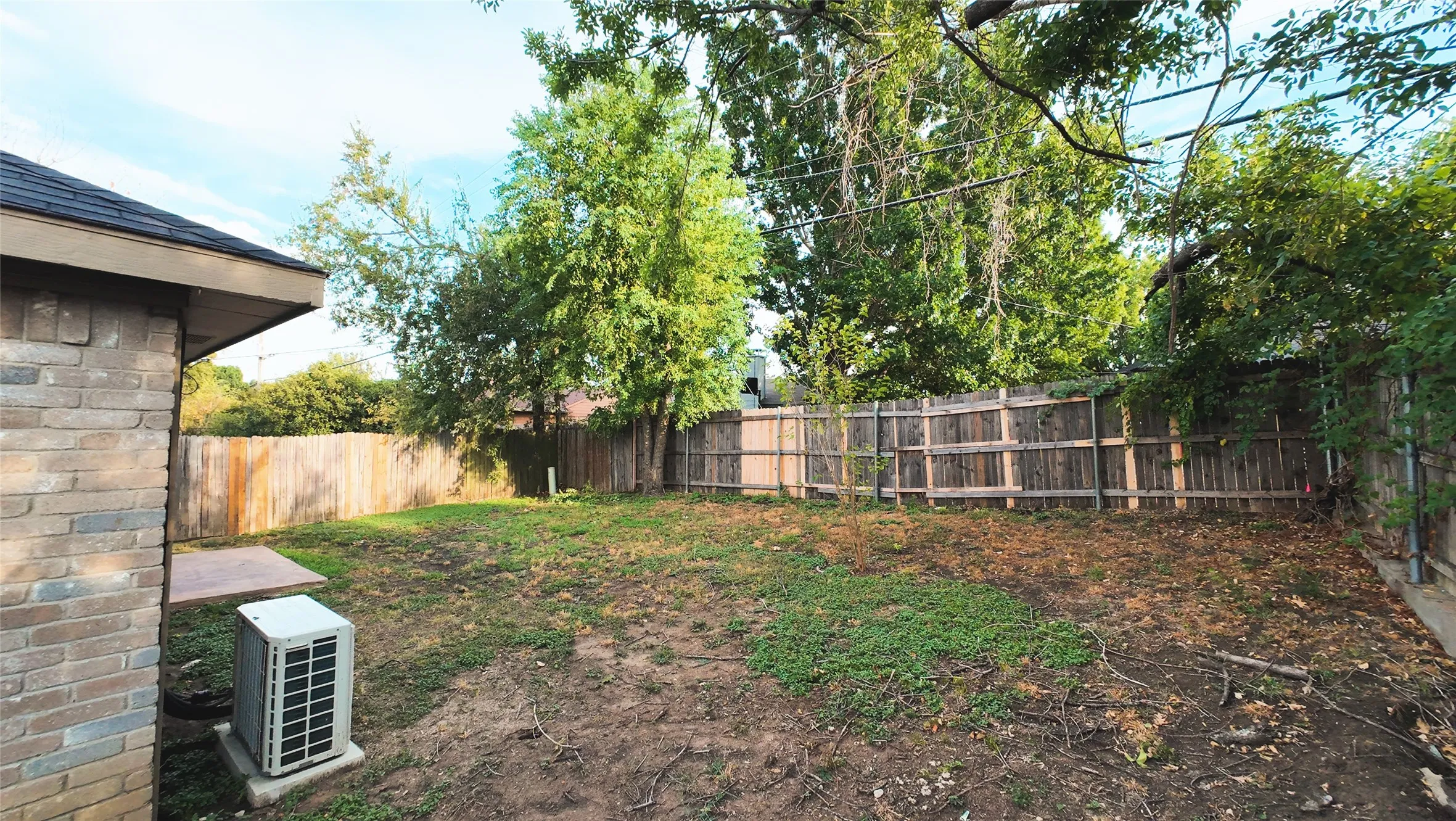 Spacious backyard with a wood privacy fence, mature trees, and a brick exterior