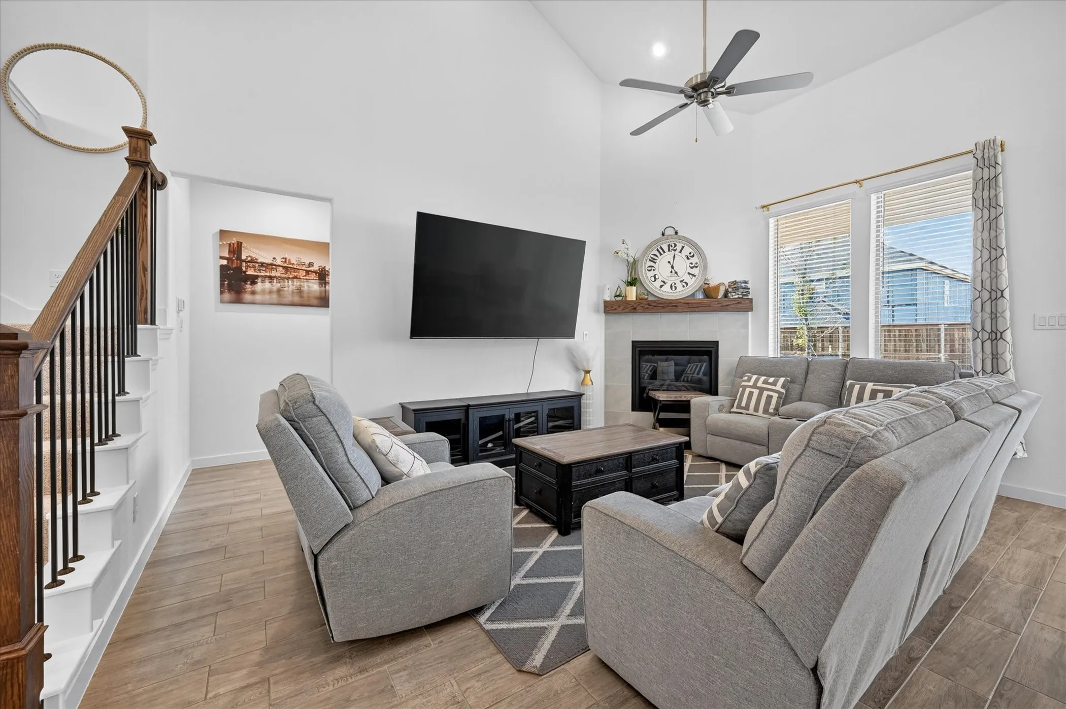 Vaulted ceilings, wood-finish flooring, corner fireplace with wood mantel, large windows with blinds, and a staircase featuring wood newel posts and metal balusters