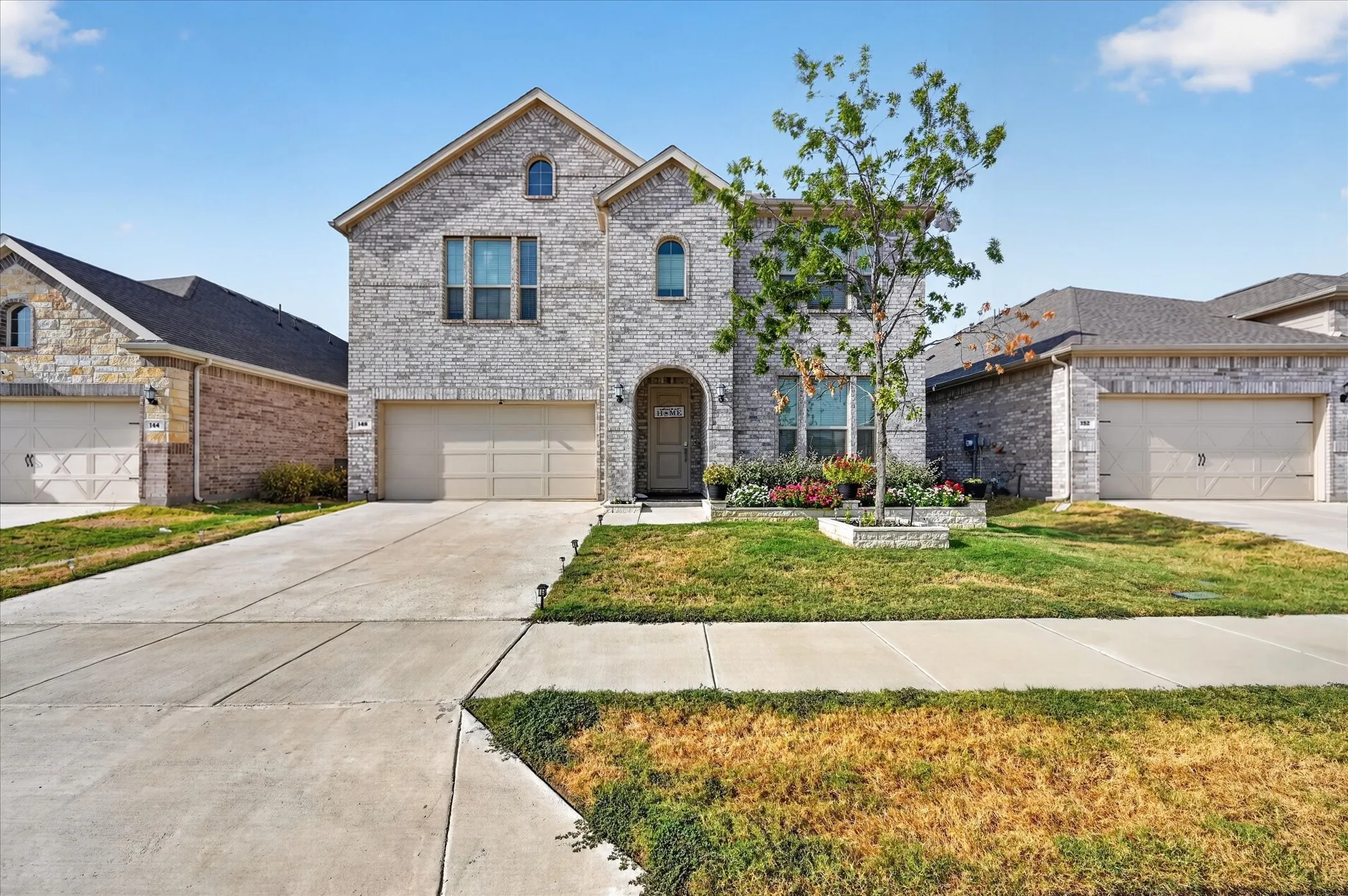 Two-story brick exterior with arched entryway, attached two-car garage, concrete driveway, and front landscaping