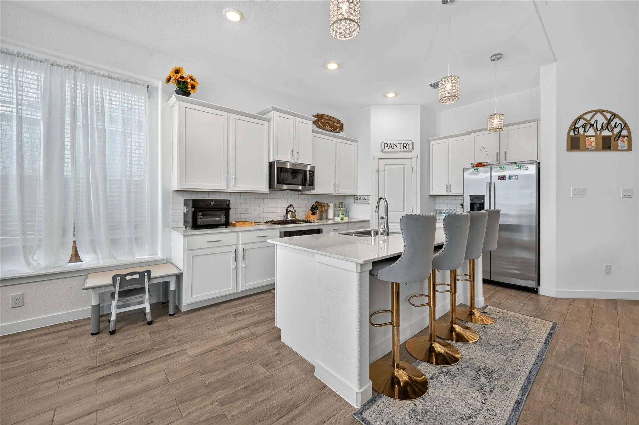 White cabinetry with brushed nickel hardware, stainless steel appliances, a center island with countertop seating, recessed lighting, and wood-finish flooring