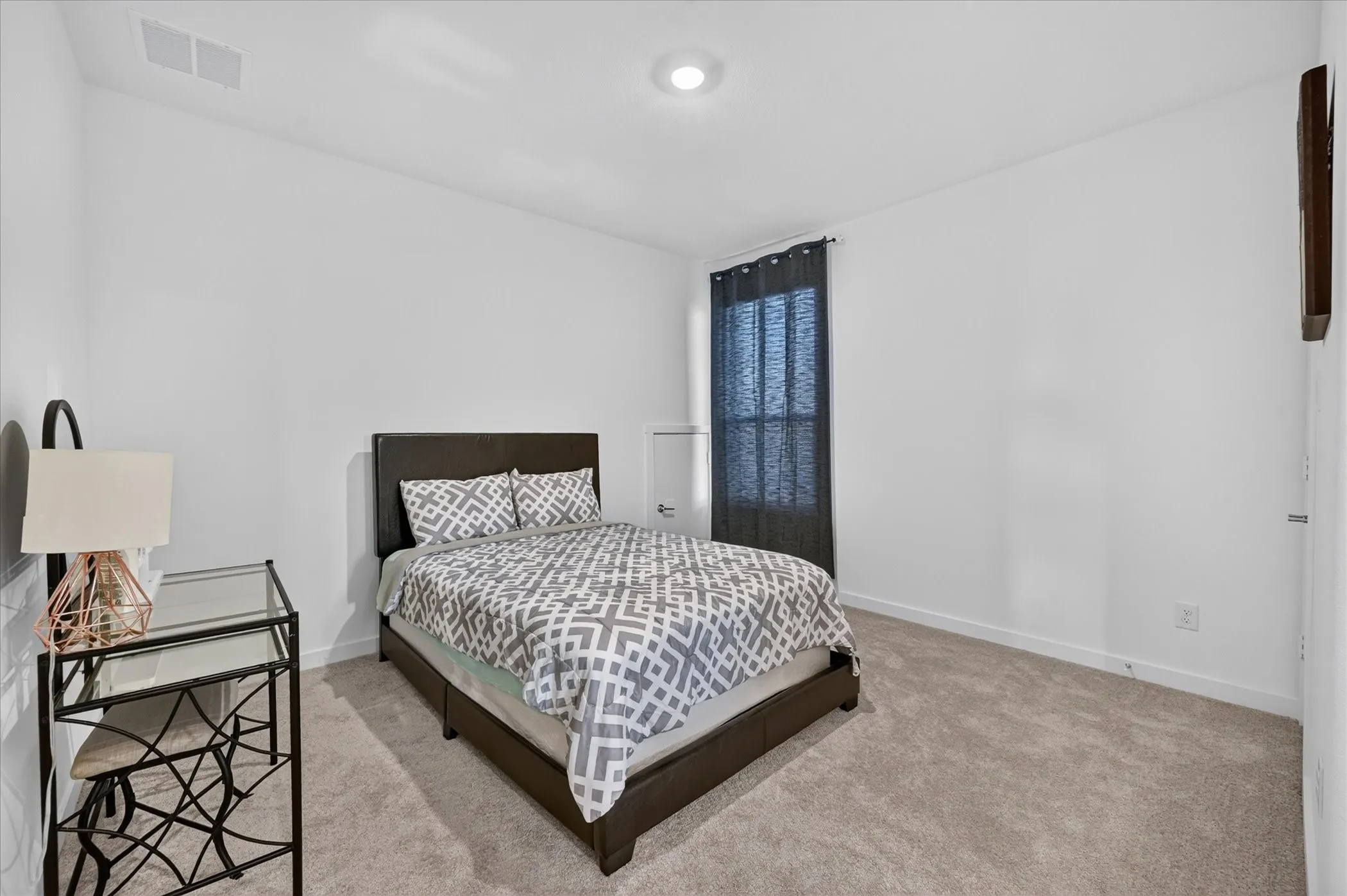 Neutral tone wall paint, carpet flooring, a window with dark curtains, and an overhead light fixture