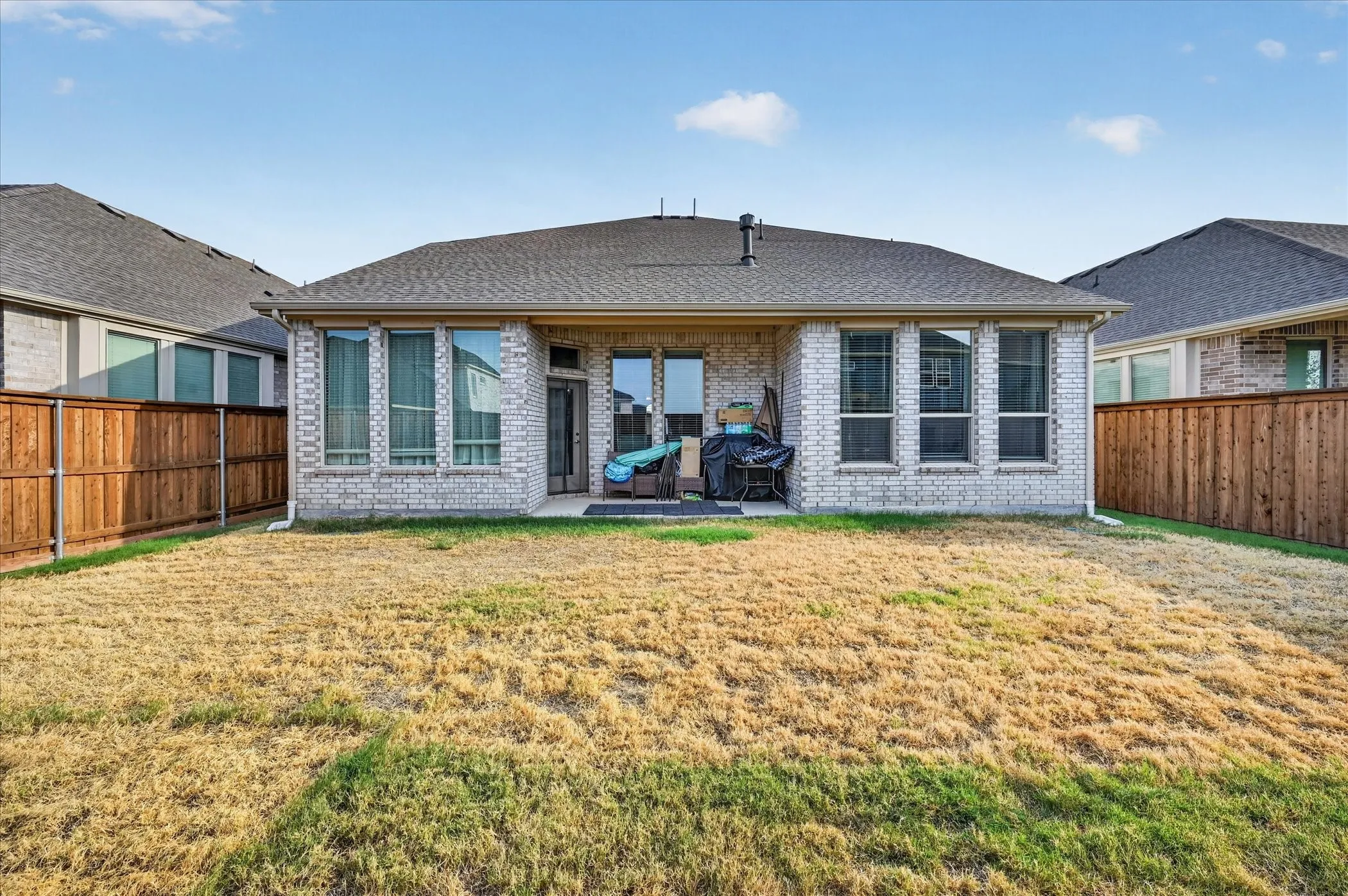 Rear exterior featuring a covered patio, brick facade, shingle roof, and privacy fencing