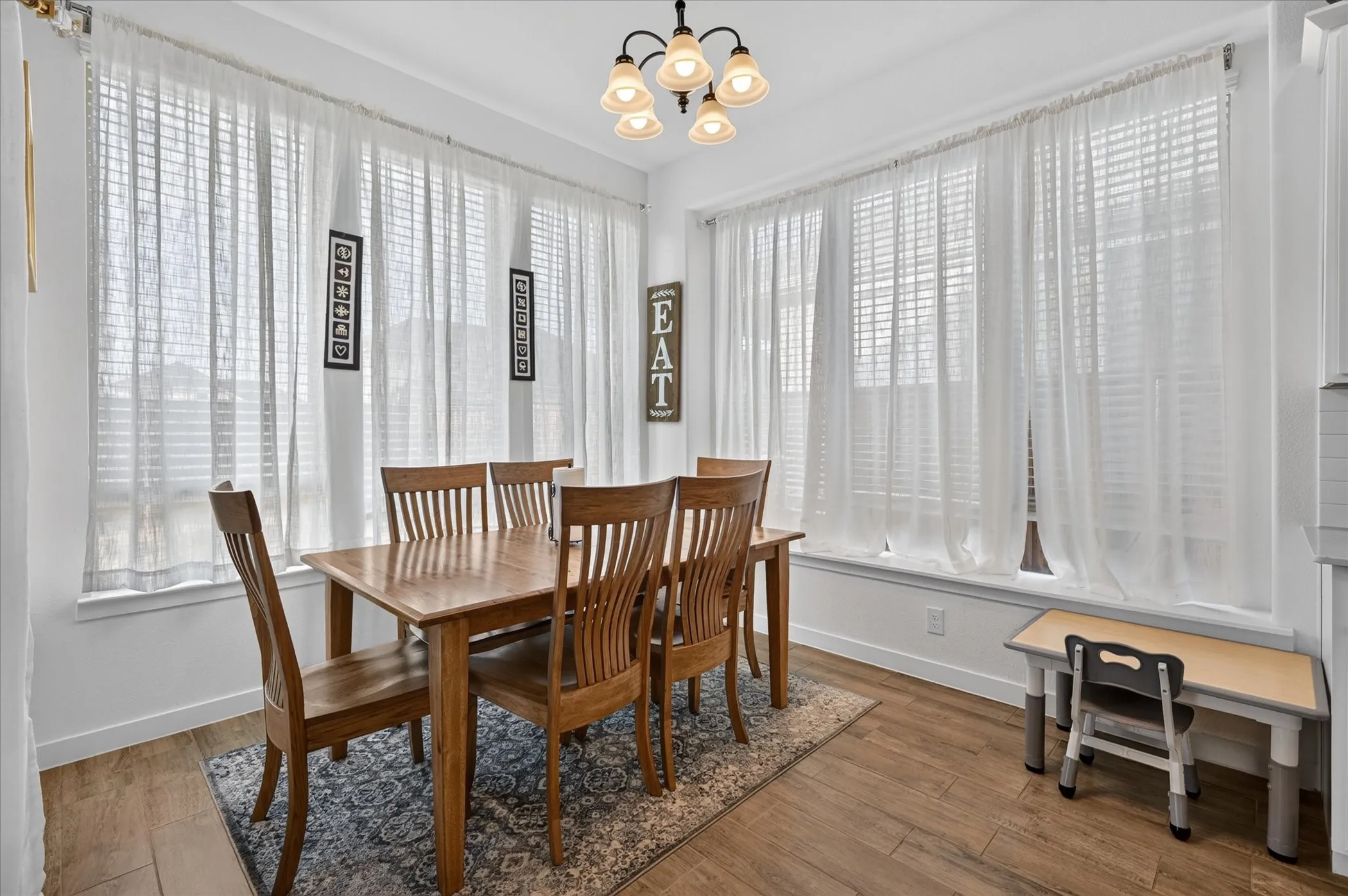 Wood-finish flooring, multiple windows with blinds, and an overhead chandelier with decorative shades