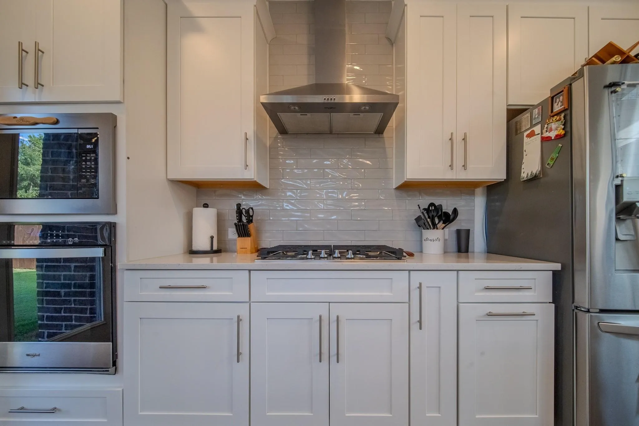 White cabinetry with stainless steel hardware, built-in microwave, integrated oven, and a gas range with an overhead exhaust hood