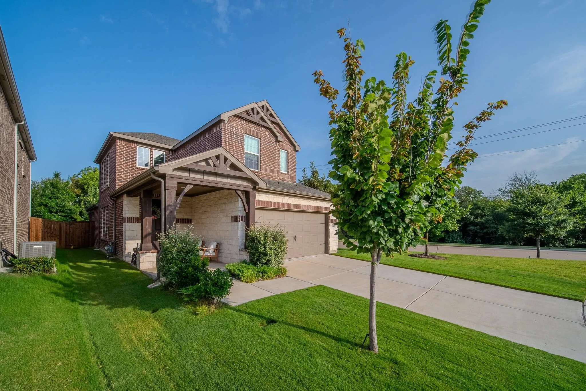 Brick exterior with stone accents, covered front porch, attached garage, concrete driveway, and established landscaping