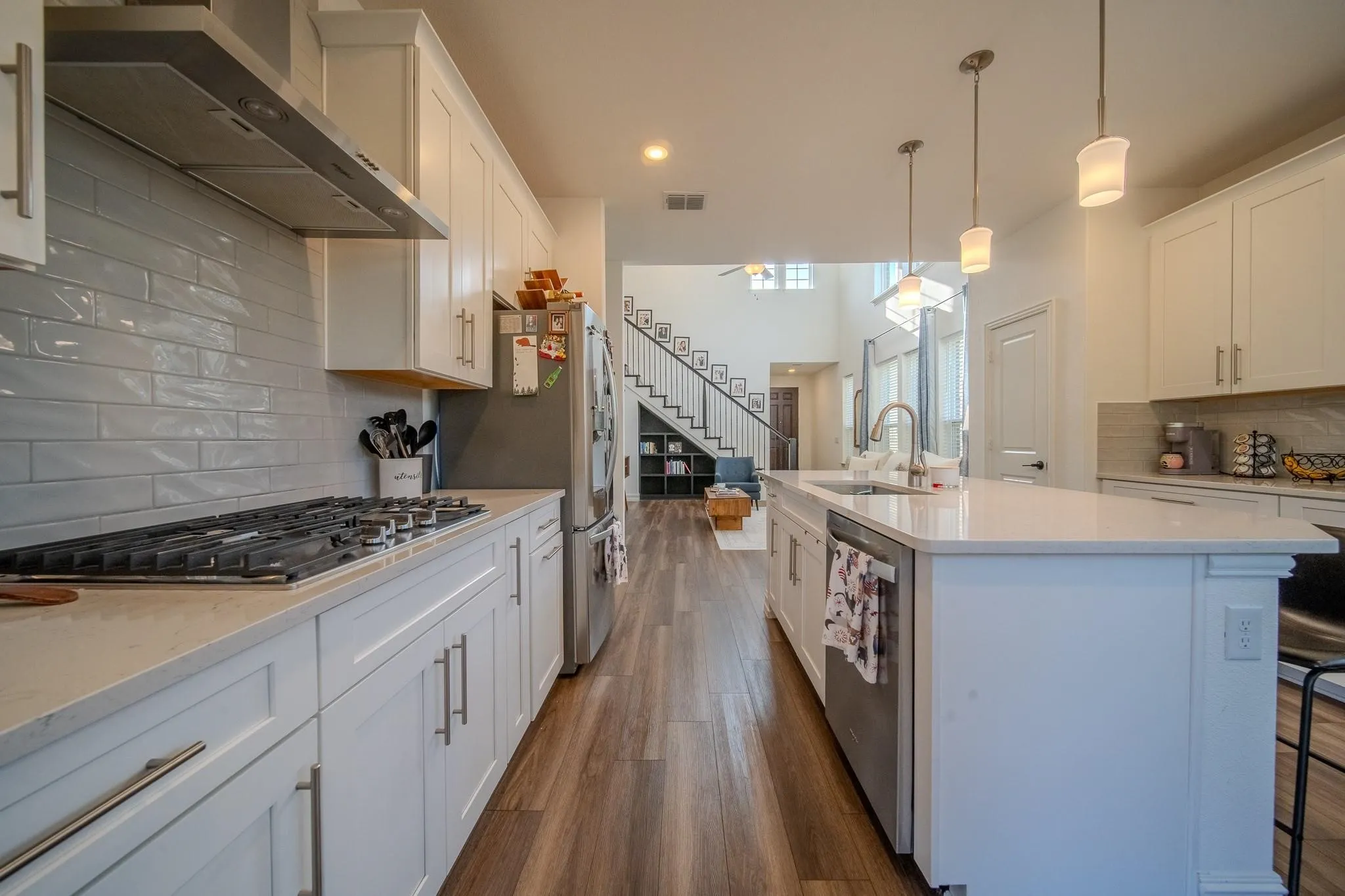 Kitchen featuring white shaker cabinetry, light-toned countertops, a gas range with stainless steel hood, a large kitchen island with pendant lighting, and wood-finish flooring